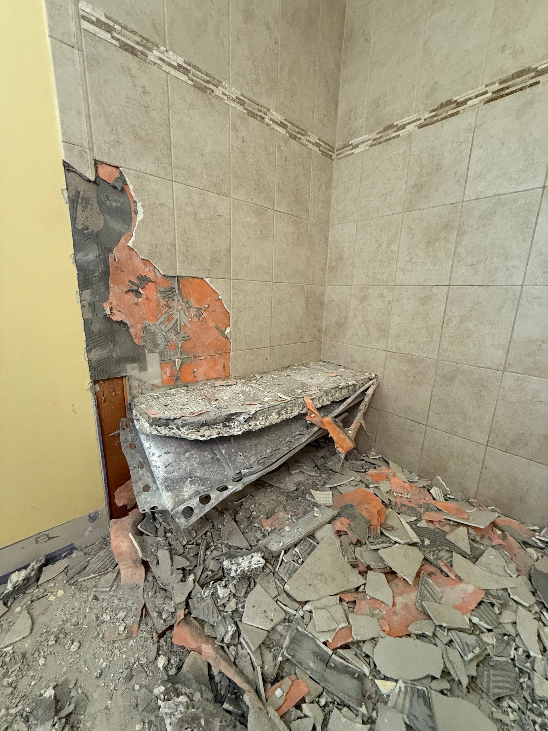 Demolition of a tiled bathroom corner; debris and exposed wall visible.
