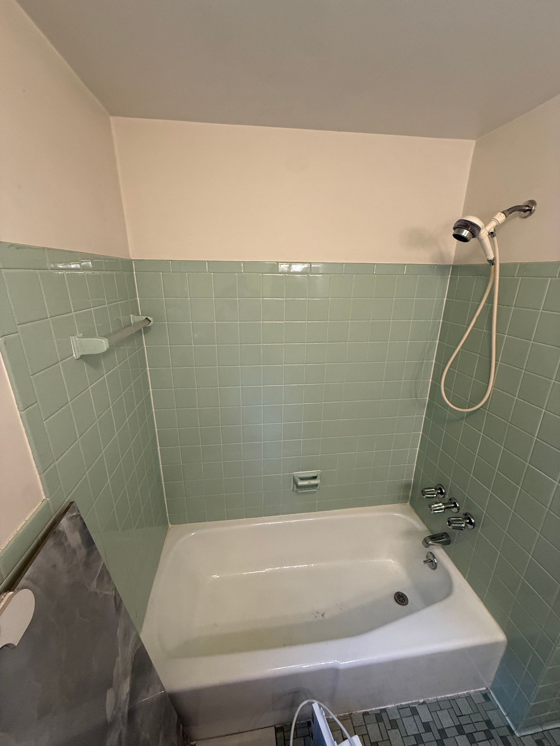 Light green tiled bathroom with a white tub and shower head. The walls are light green, and the ceiling is off-white.