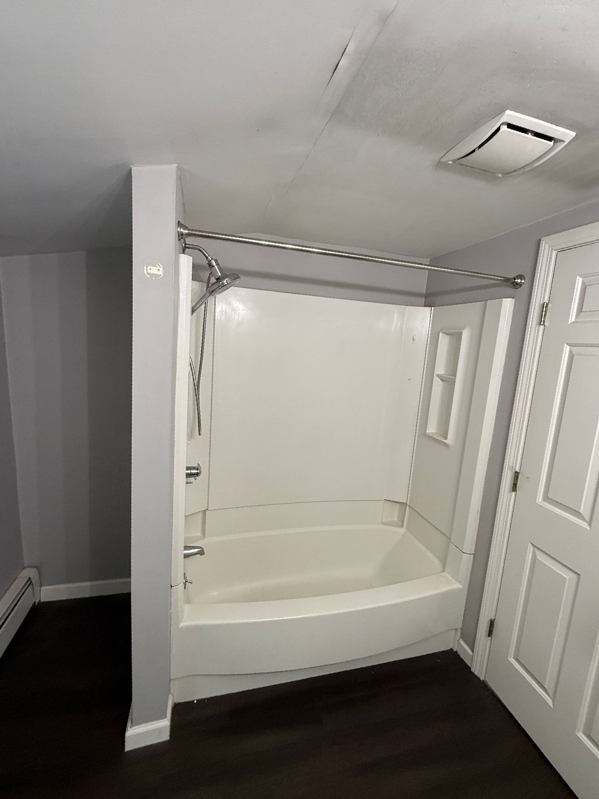Bathroom with a white tub and shower, grey walls, and dark flooring.