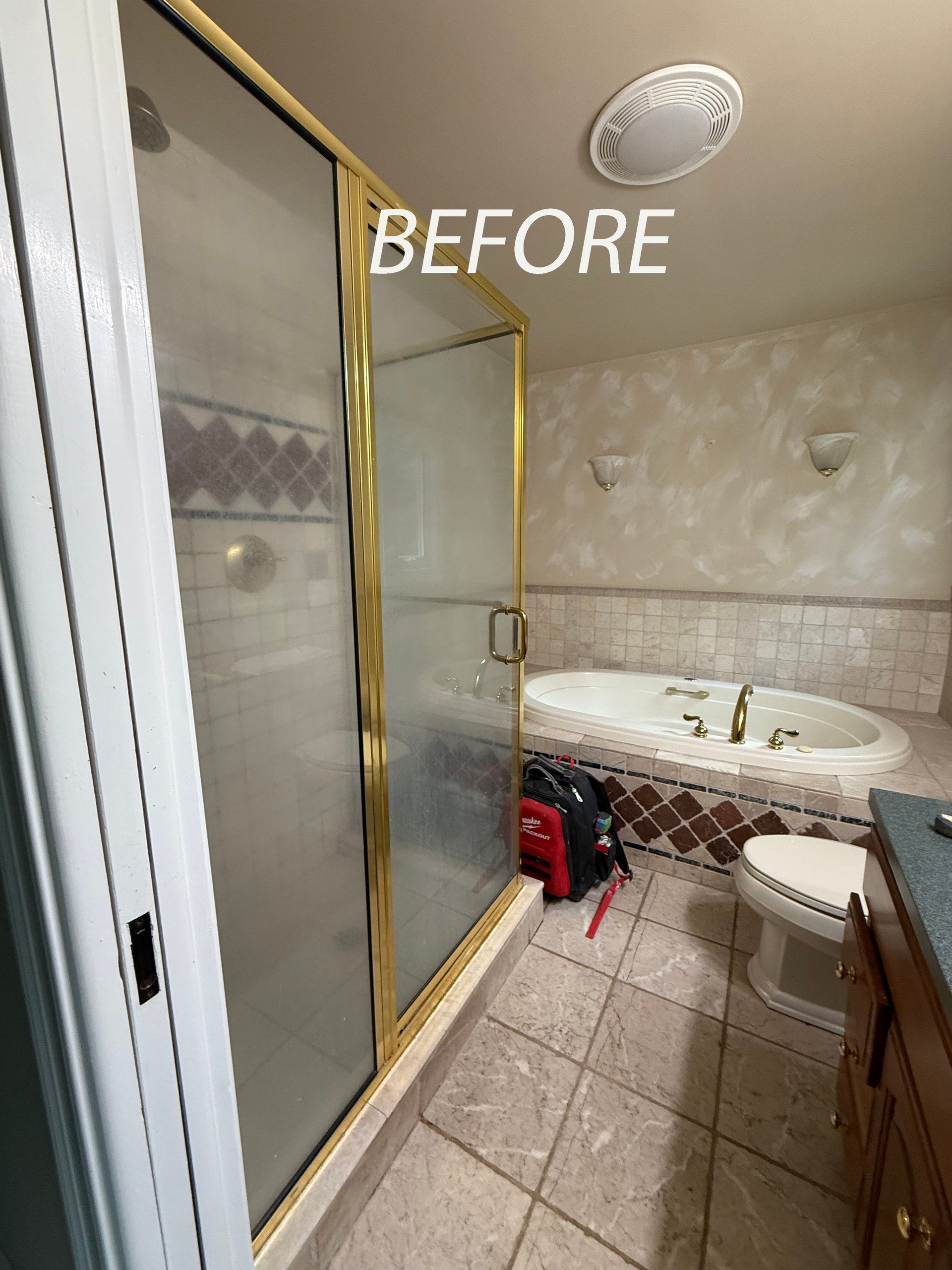 Bathroom with gold-framed shower, tub, toilet, vanity, and tile floor, before renovation.