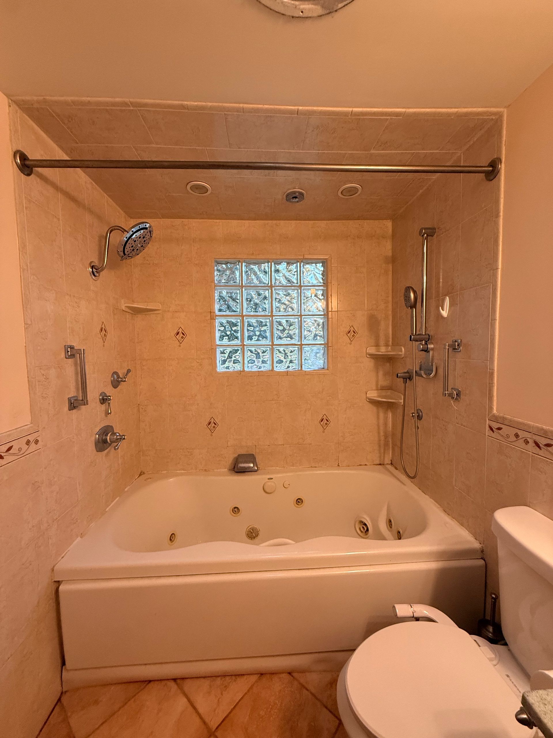 Berlin CT bathroom with a white jacuzzi tub, shower, and toilet, tan tile, glass block window, and grab bars.