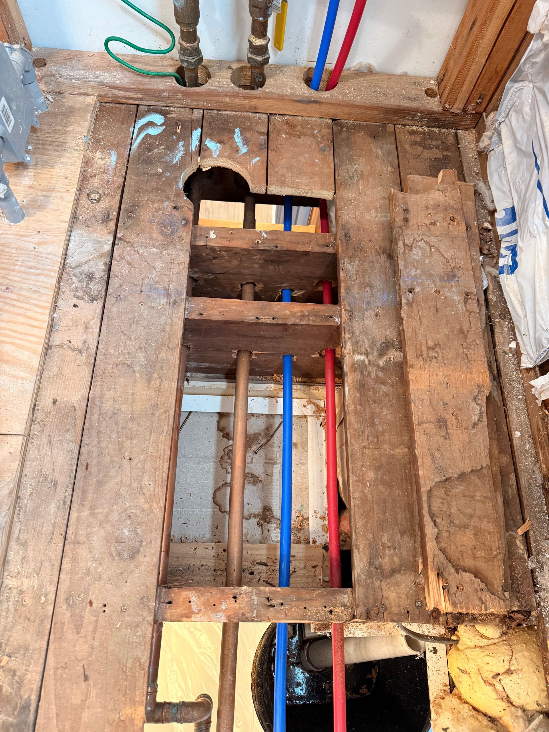 Bathroom remodel in progress: Exposed subfloor with plumbing, including blue and red pipes, and water lines.