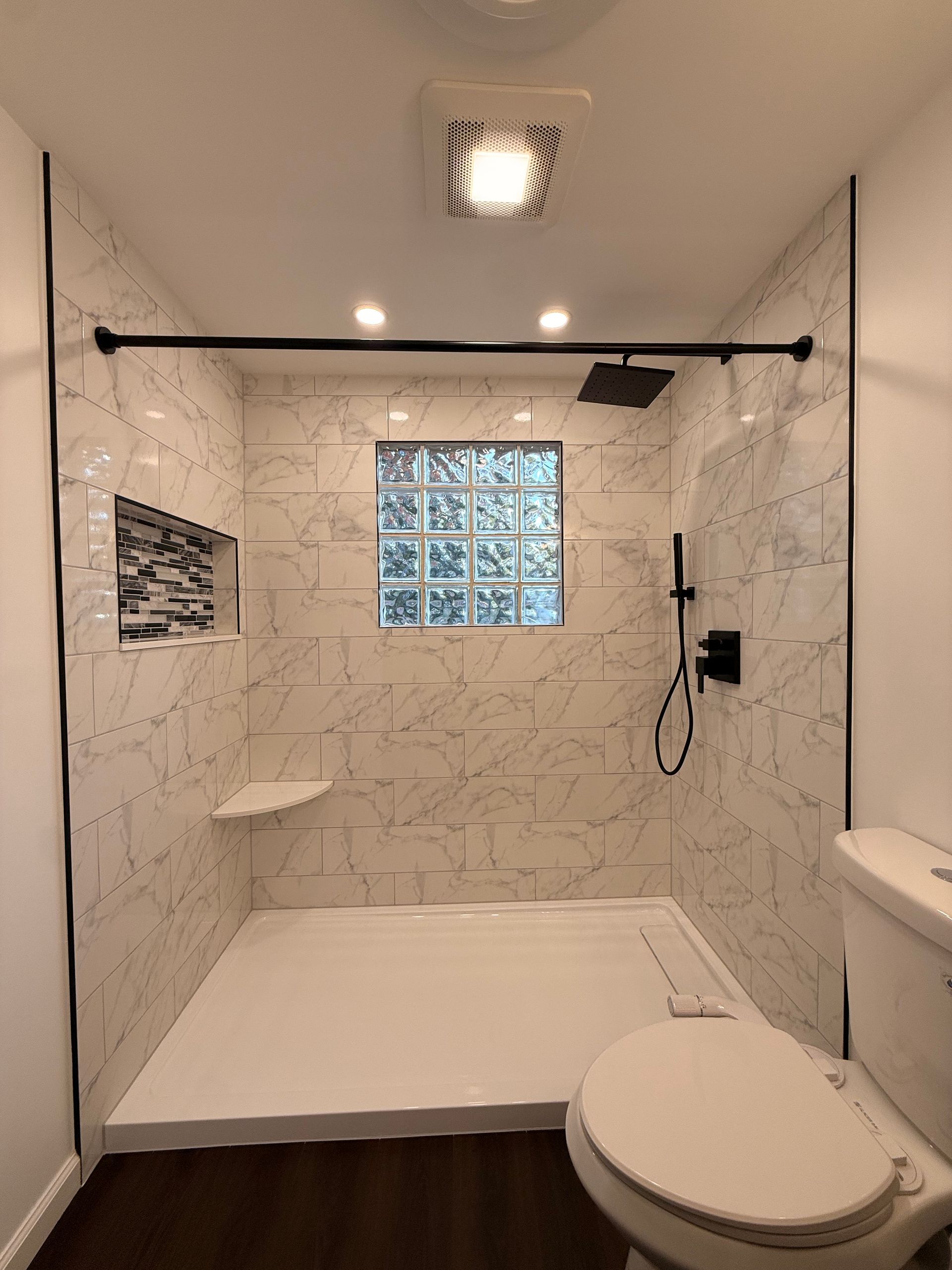 Southington CT Bathroom with a white bathtub and shower with marble-look tile walls. A recessed shelf features mosaic tile.