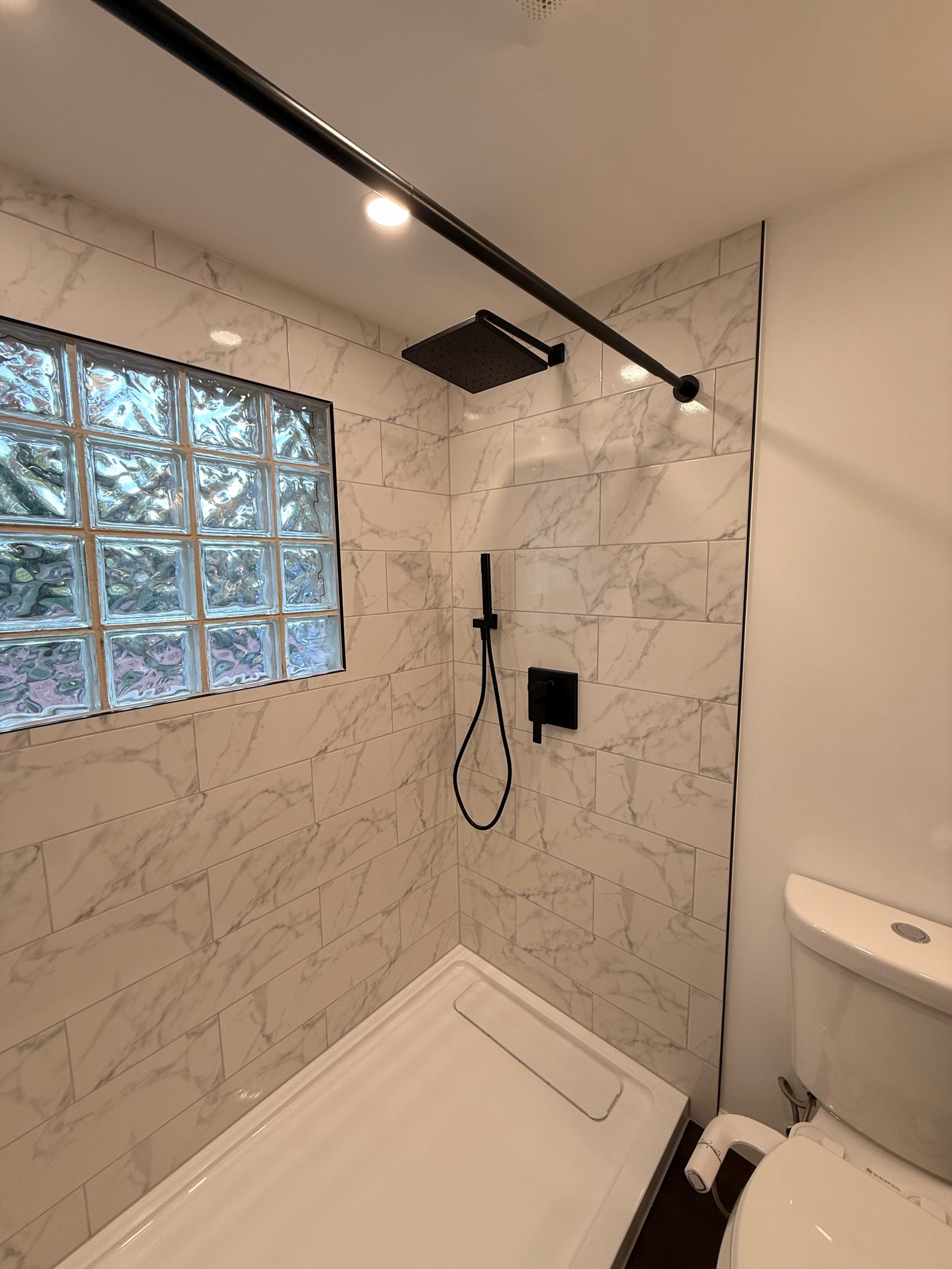 Modern Berlin shower with marble tile, black fixtures, and a glass block window.