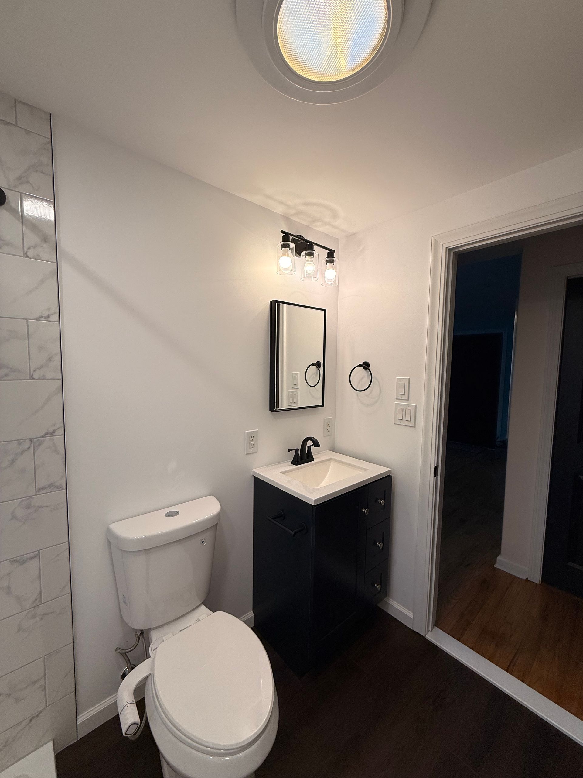 Small Berlin bathroom with toilet, sink, mirror, and a dark blue door. Light-colored walls and floor, and an overhead skylight.