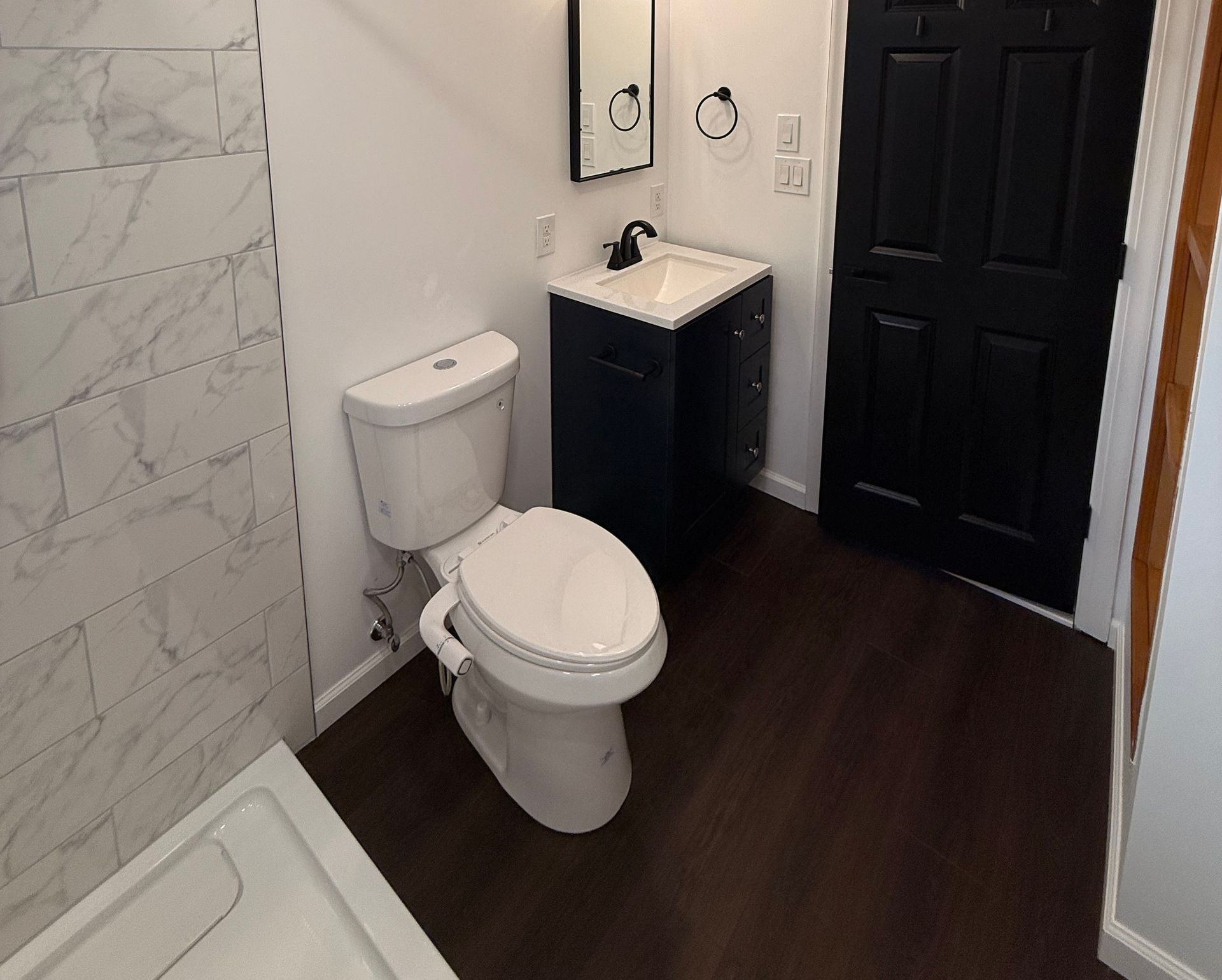 Berlin bathroom with white marble shower, black door and fixtures, and dark wood flooring.