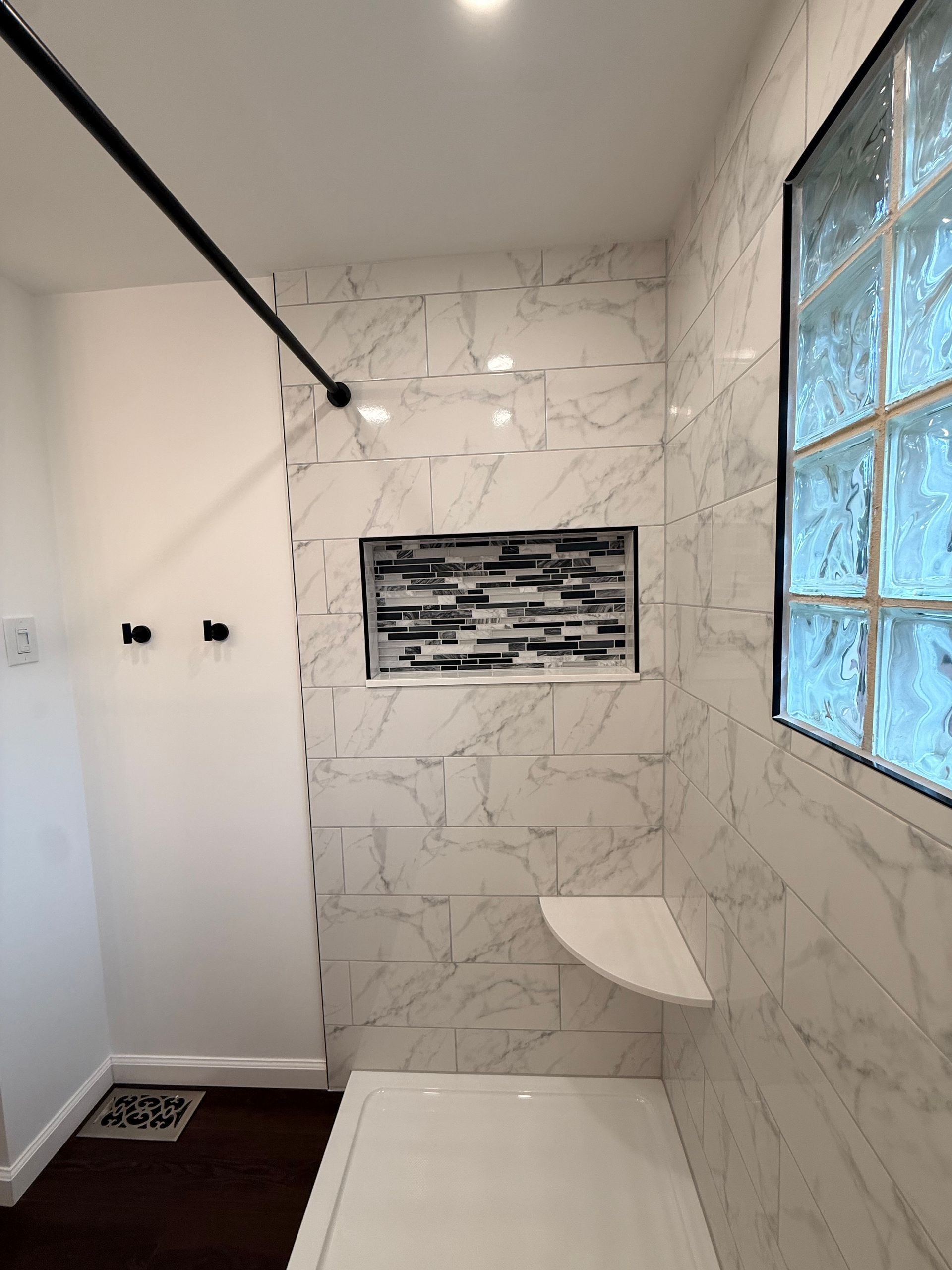 Berlin bathroom with white marble-like tile, built-in shelf, shower niche, and glass block window.