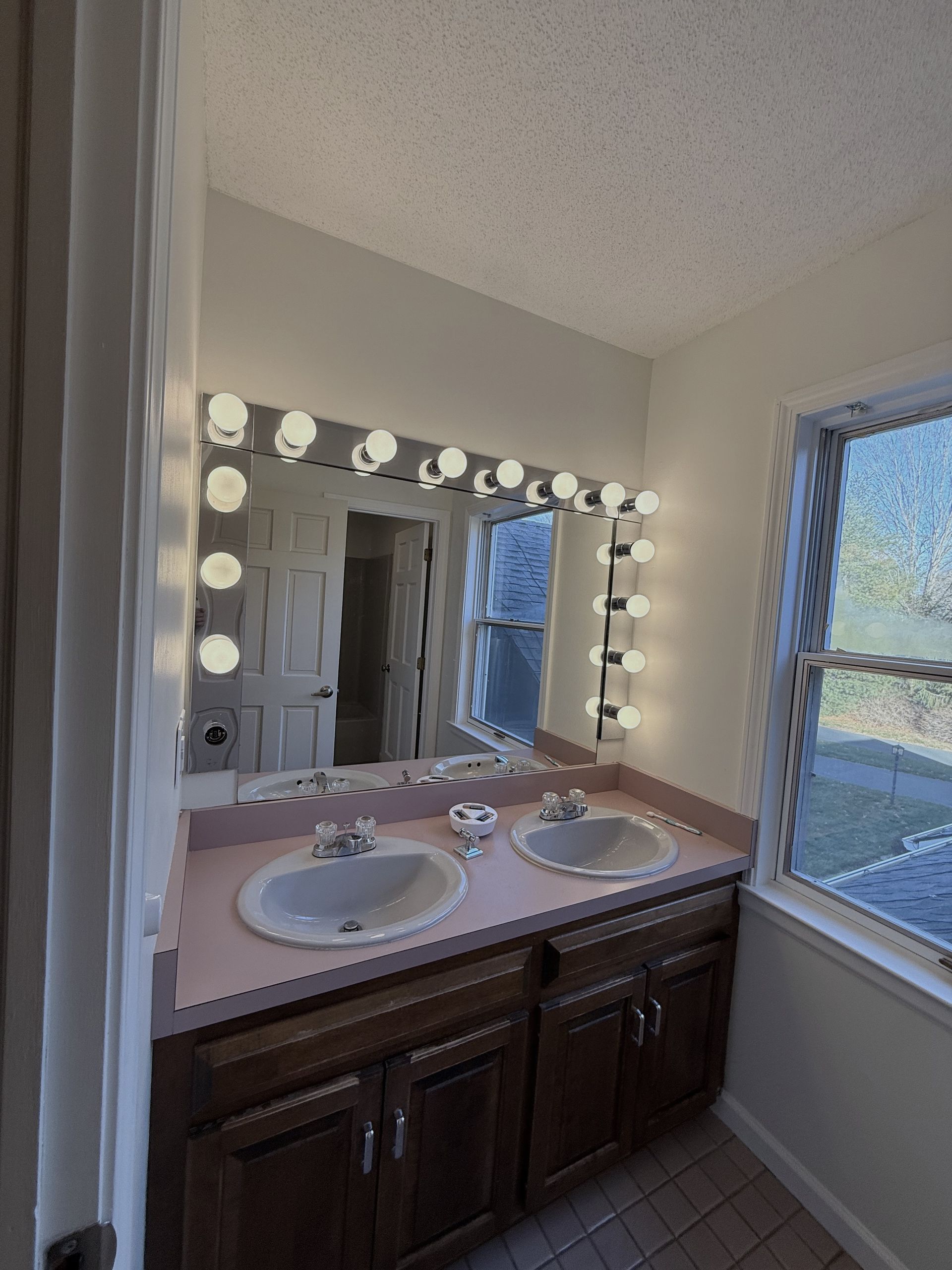 Bristol bathroom with double sinks, large mirror with lightbulbs, and a window.