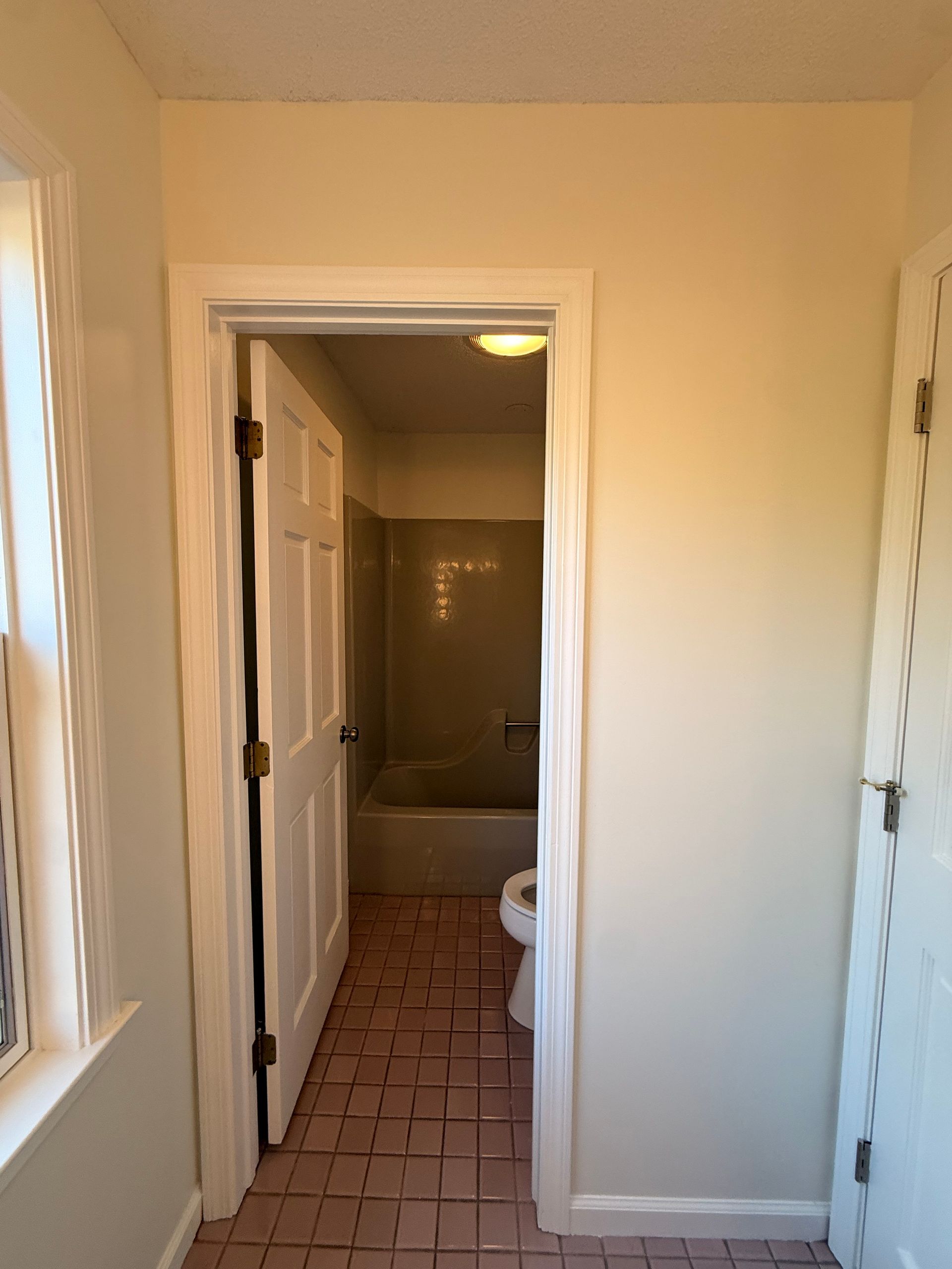Hallway with doorway to Bristol bathroom. Pink tile floor, white door, beige walls.