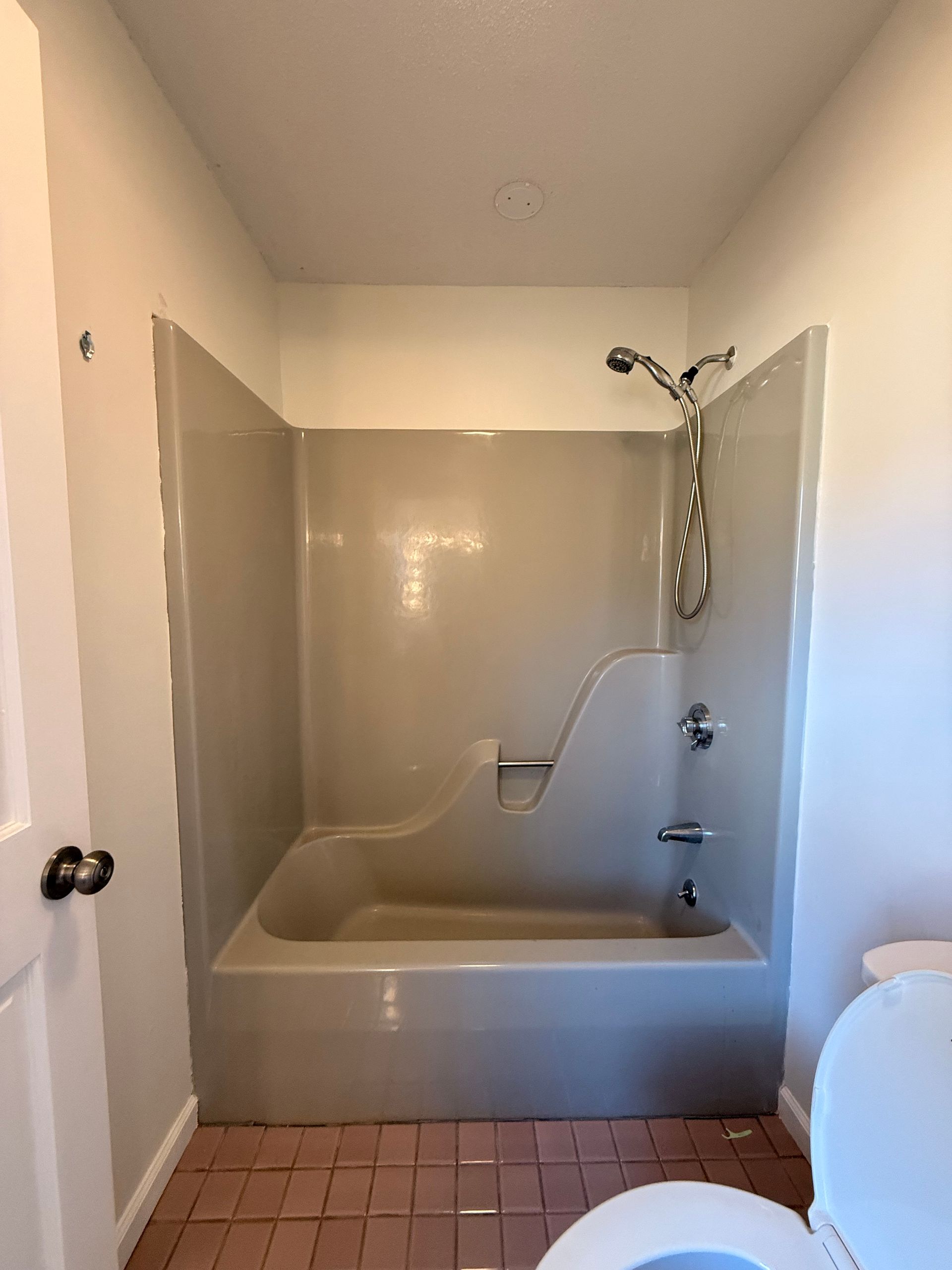 Small bathroom in Bristol, CT with with beige tub/shower unit, white walls, and pink tile floor.