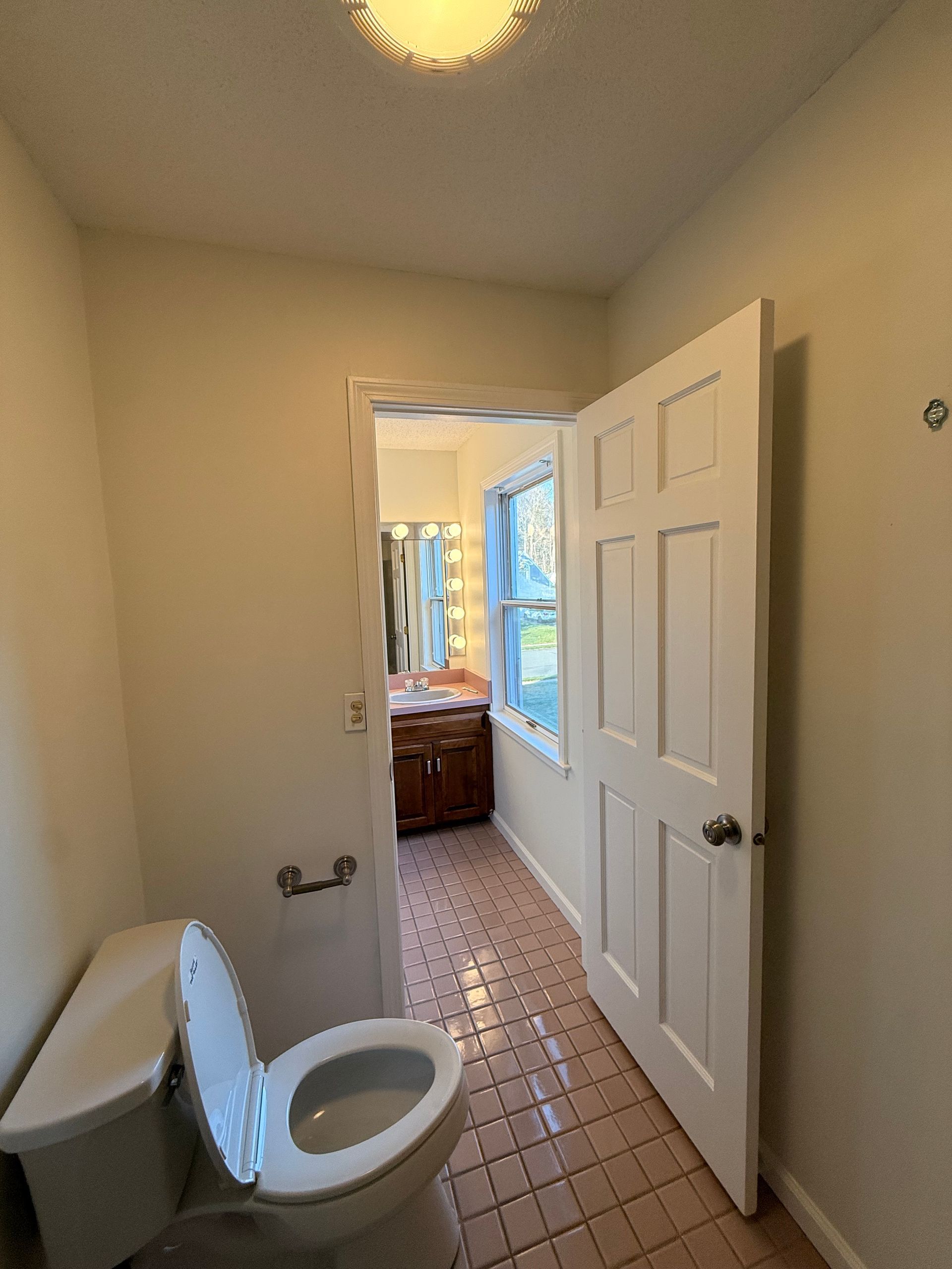 Bristol Bathroom with open door to a vanity, toilet in the foreground. Pink tiled floor, white walls and trim.