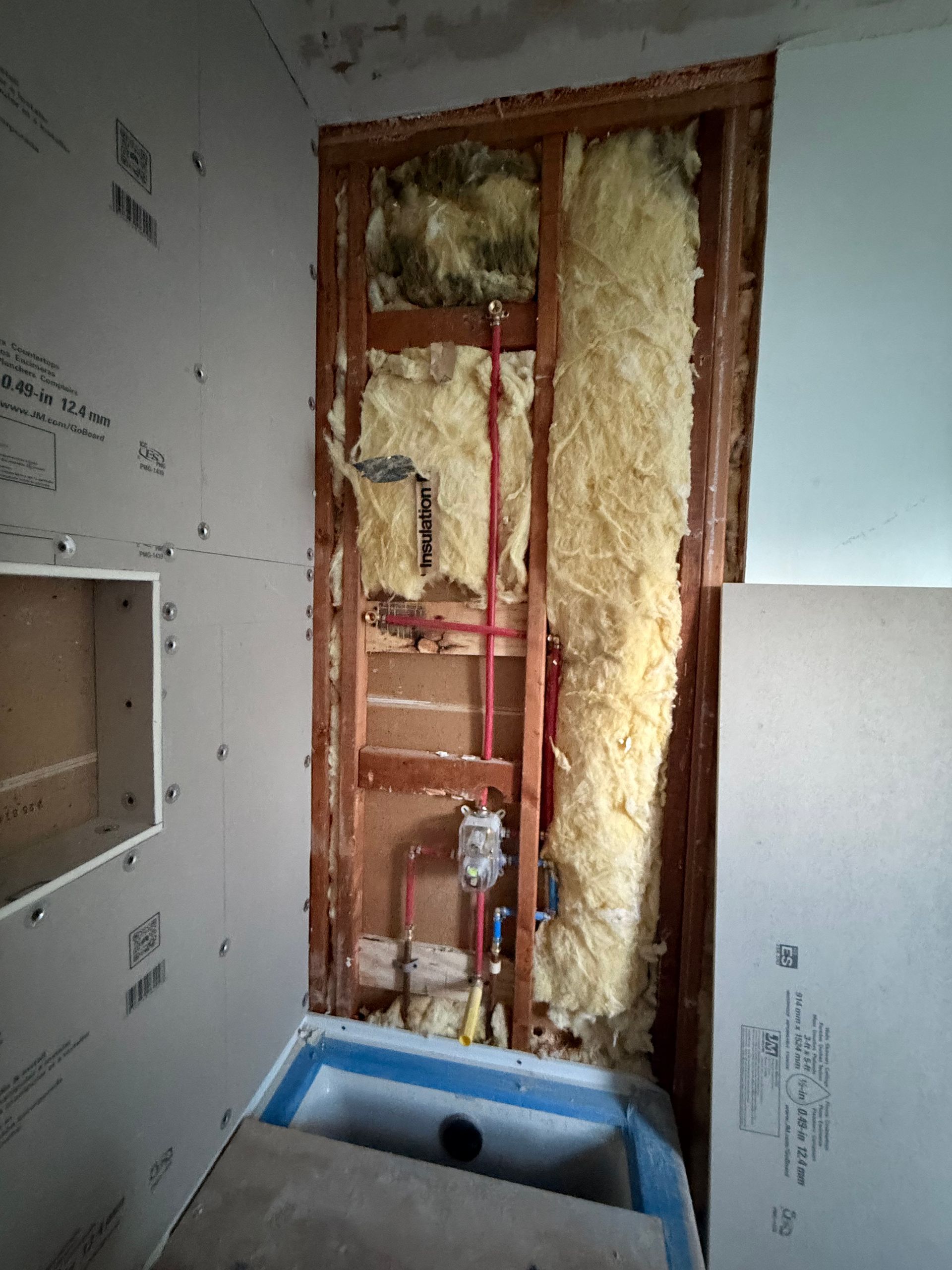 Bathroom remodel in progress: exposed plumbing, insulation, cement board, and a blue tub.