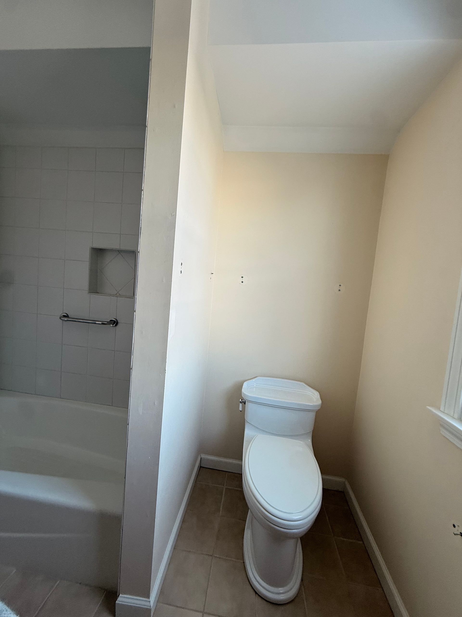 A view of a bathroom showing a toilet in a small alcove next to a bathtub with white tile walls.