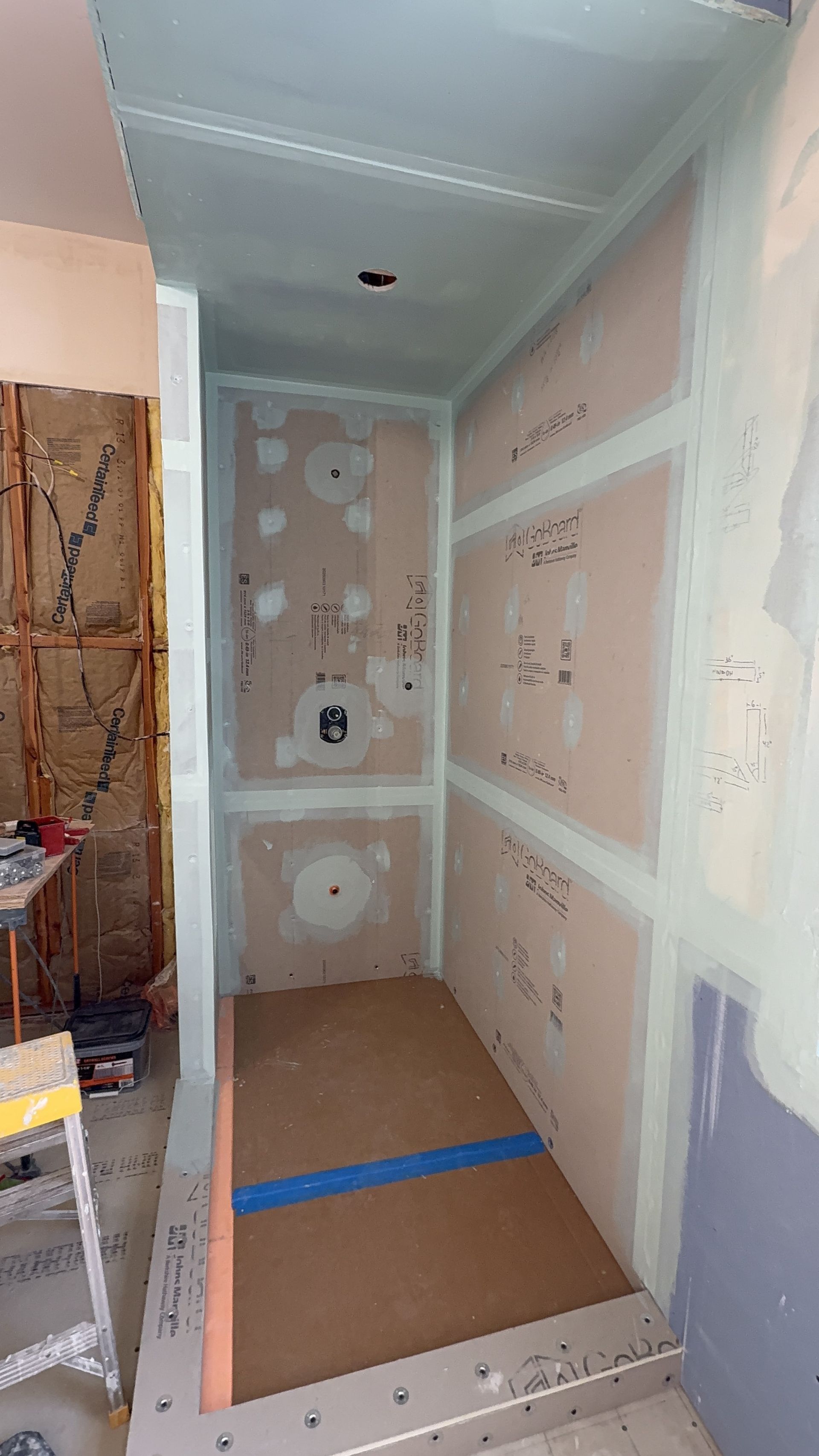 Narrow unfinished hallway with drywall panels, taping seams, and construction materials on the floor.