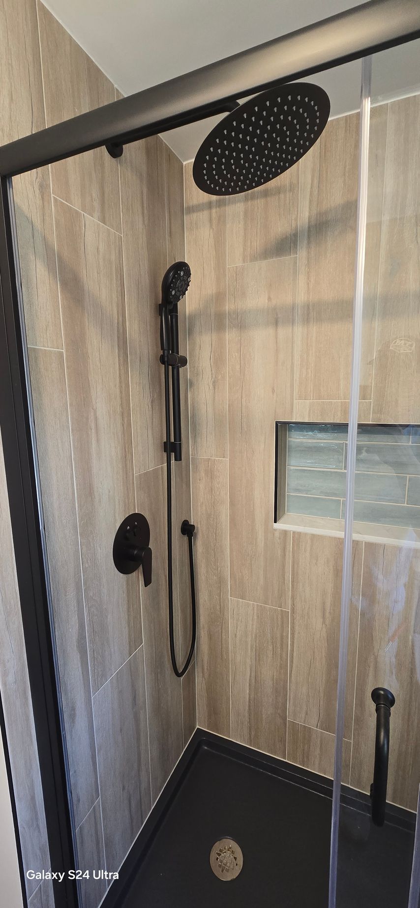 A shower with a black shower head and a black shower door.