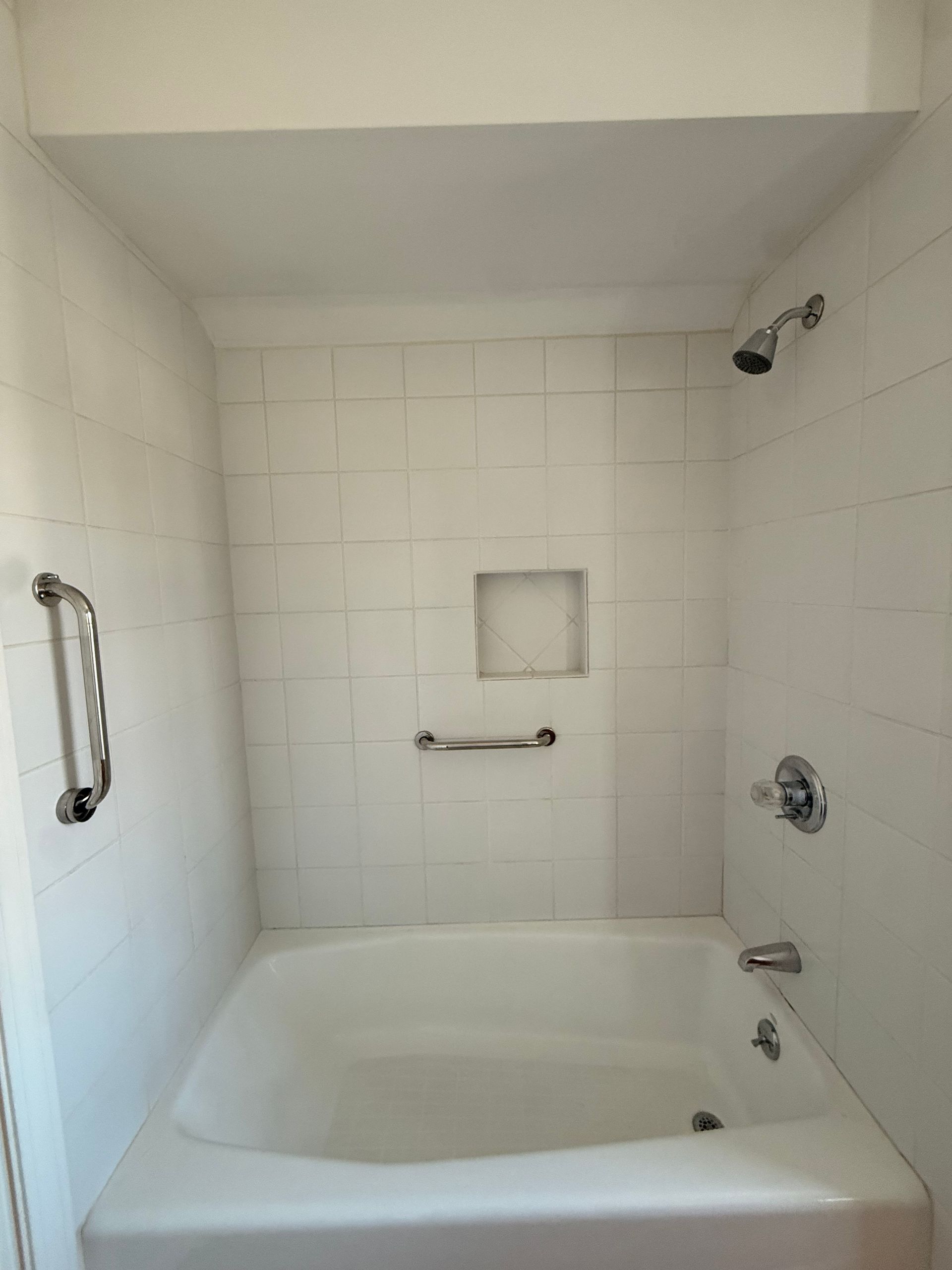 A white bathtub in Cromwell, CT with white tiled walls, including a shower head, faucet, and two silver safety grab bars.
