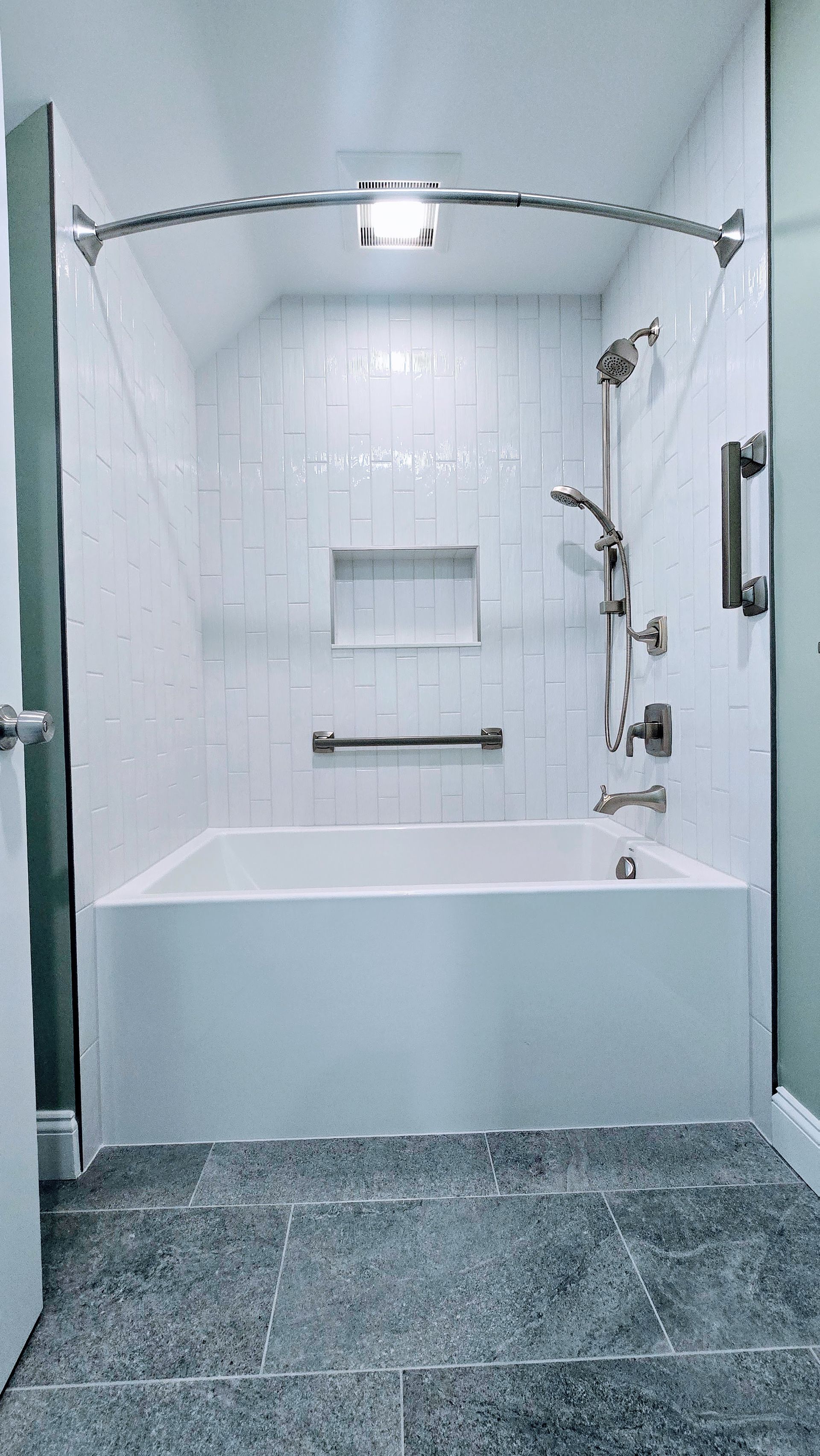 White tiled bathtub in Cromwell, CT with grab bars, showerhead, and a curved shower rod. Gray floor.