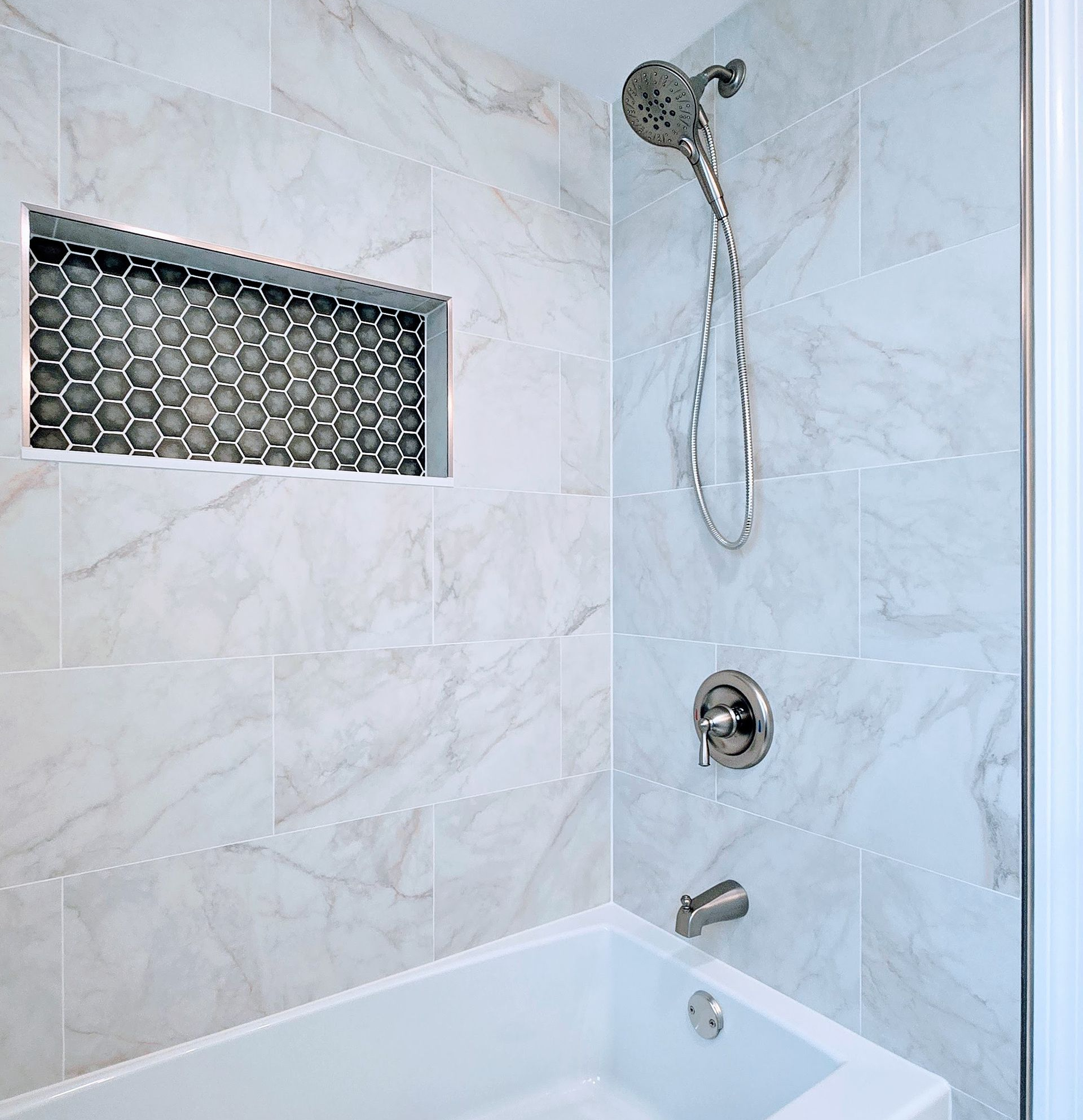 White tiled Southington CT bathroom with a bathtub, showerhead, and storage niche.