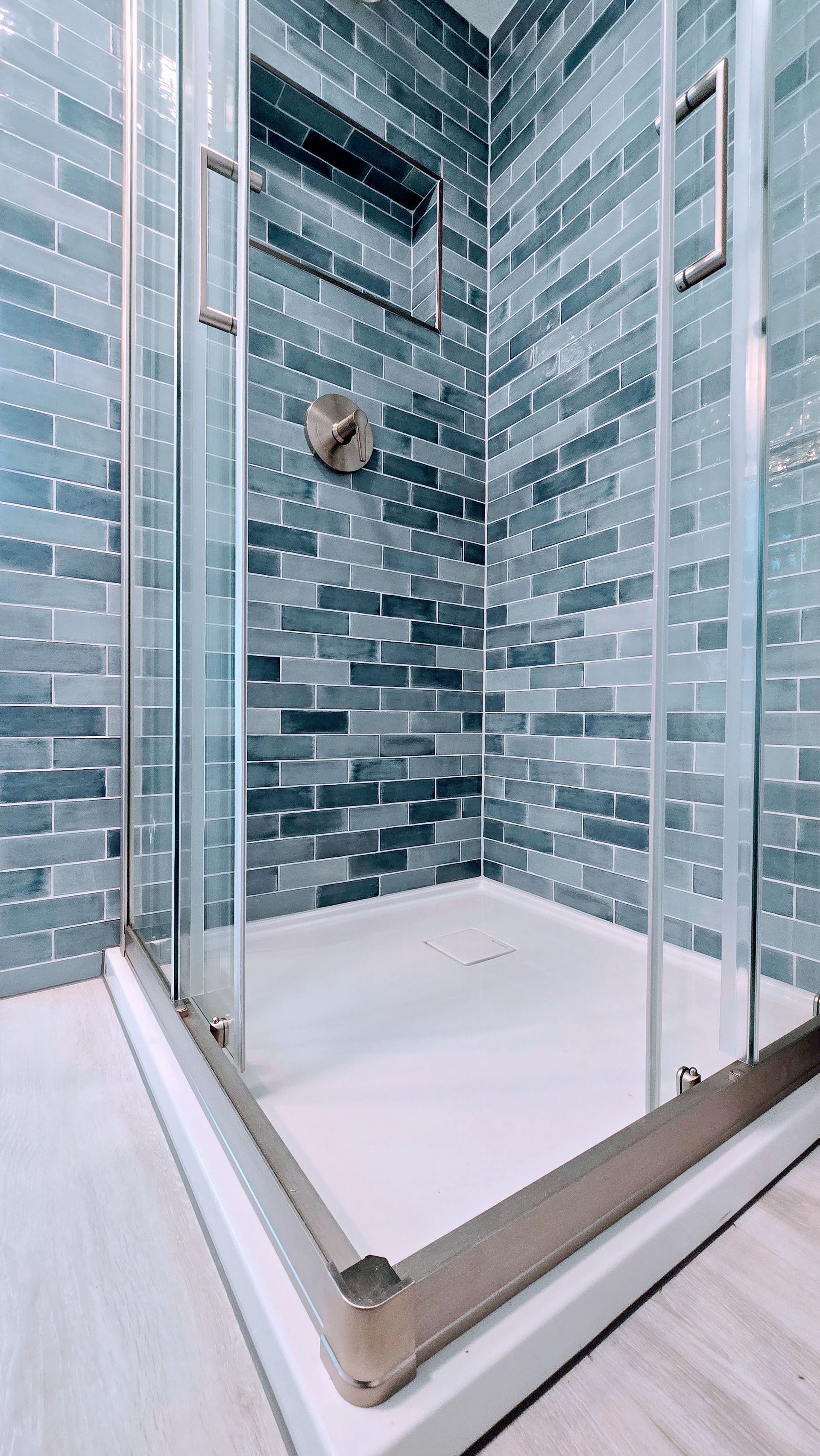 Glass-enclosed shower in Farmington, CT with blue mosaic tile walls. White shower base and light-colored flooring.