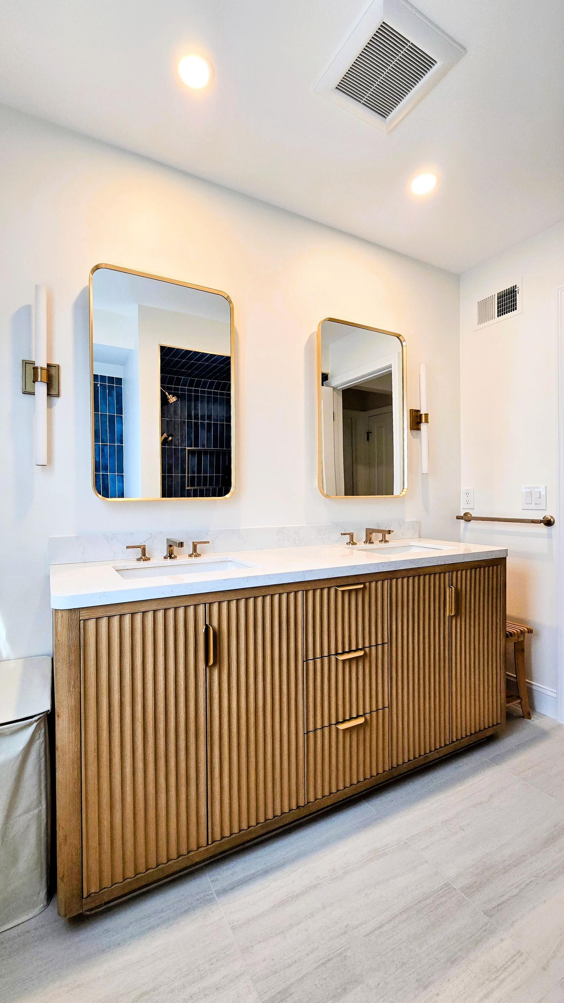 A double vanity in Cromwell, CT with a textured wood cabinet, white countertop, two mirrors, and gold fixtures in a modern bathroom.