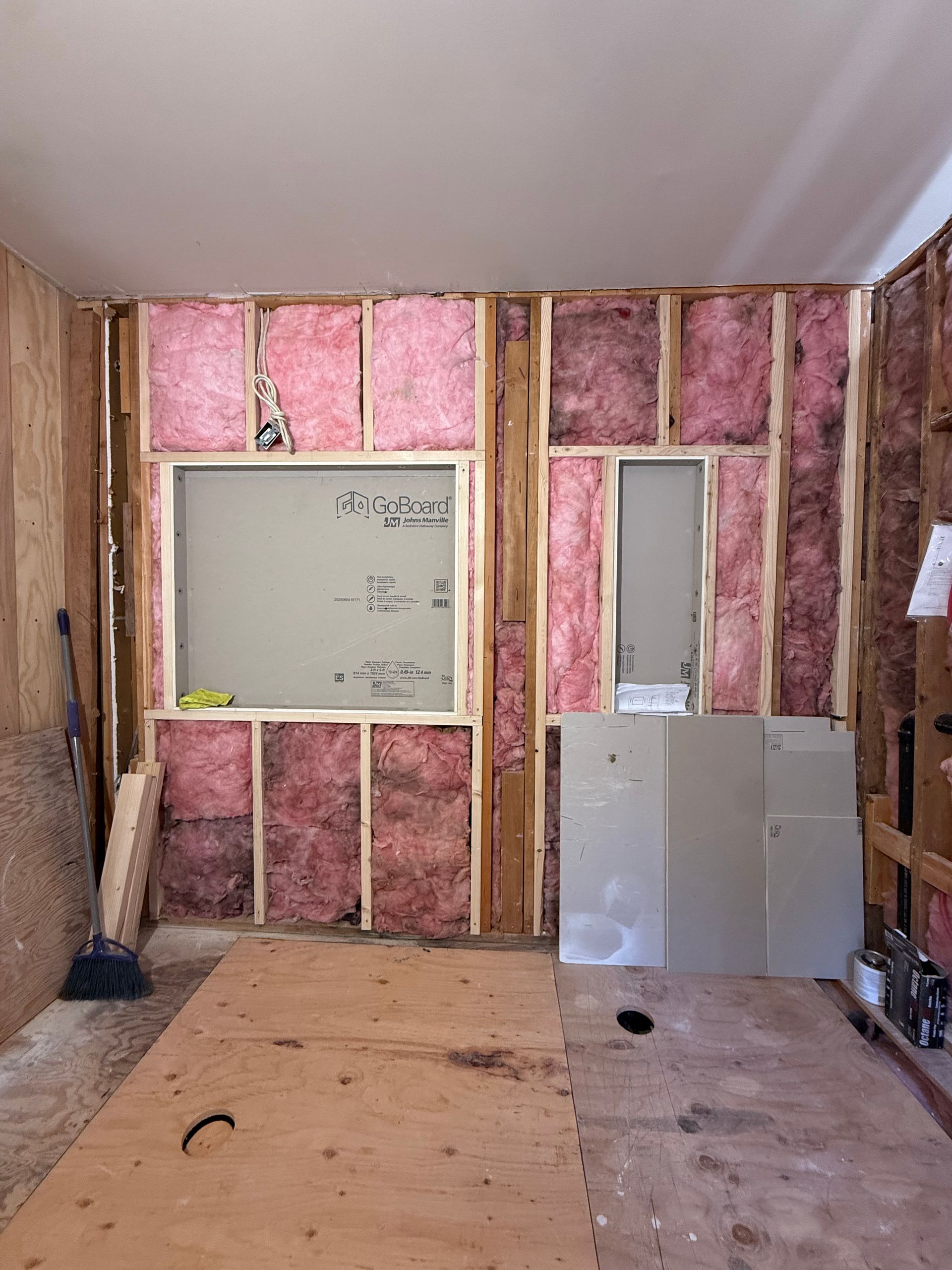 Bathroom renovation in progress in Farmington, CT; exposed pink insulation, plywood floor, and drywall on the walls.