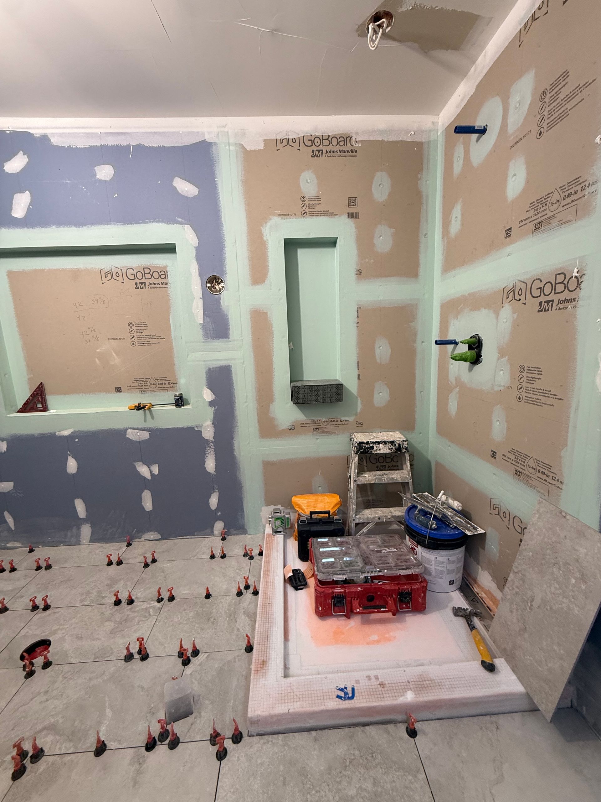 Bathroom renovation in progress, walls with cement board, floor with tile spacers, tools visible.