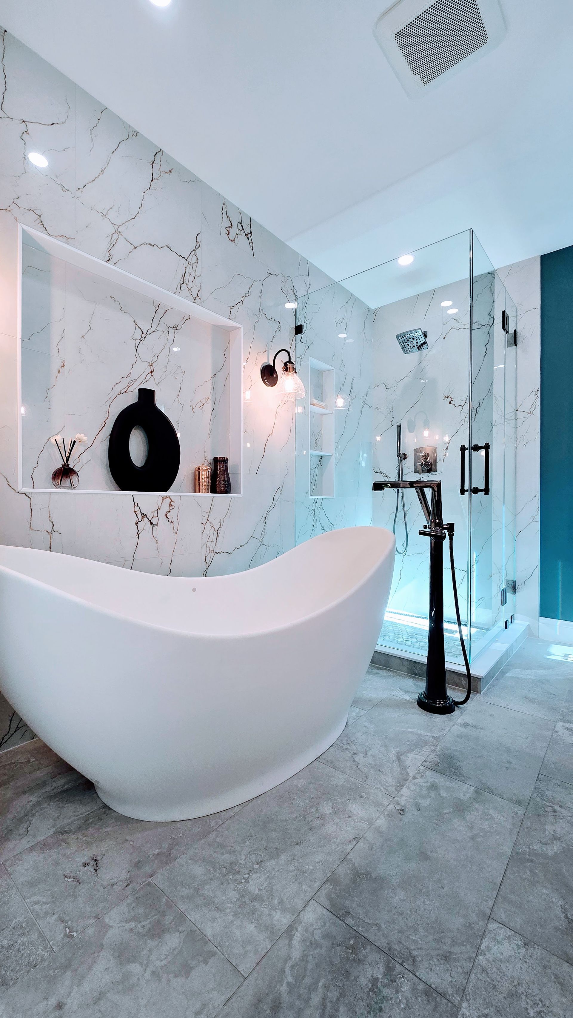 A bathroom remodel in Avon, CT featuring a teal accent wall, marble-tiled shower, freestanding tub, and a wooden vanity with granite top.