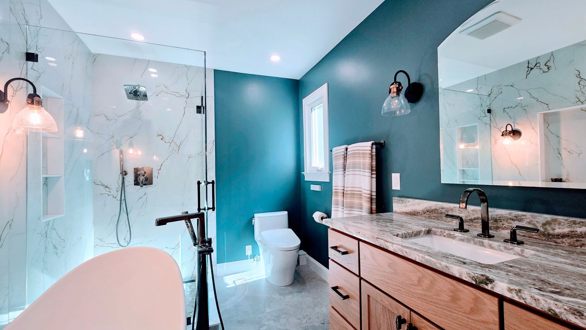 A modern bathroom in Avon, CT featuring a white soaking tub, marble walls with a built-in niche, a glass shower, and a teal accent wall.