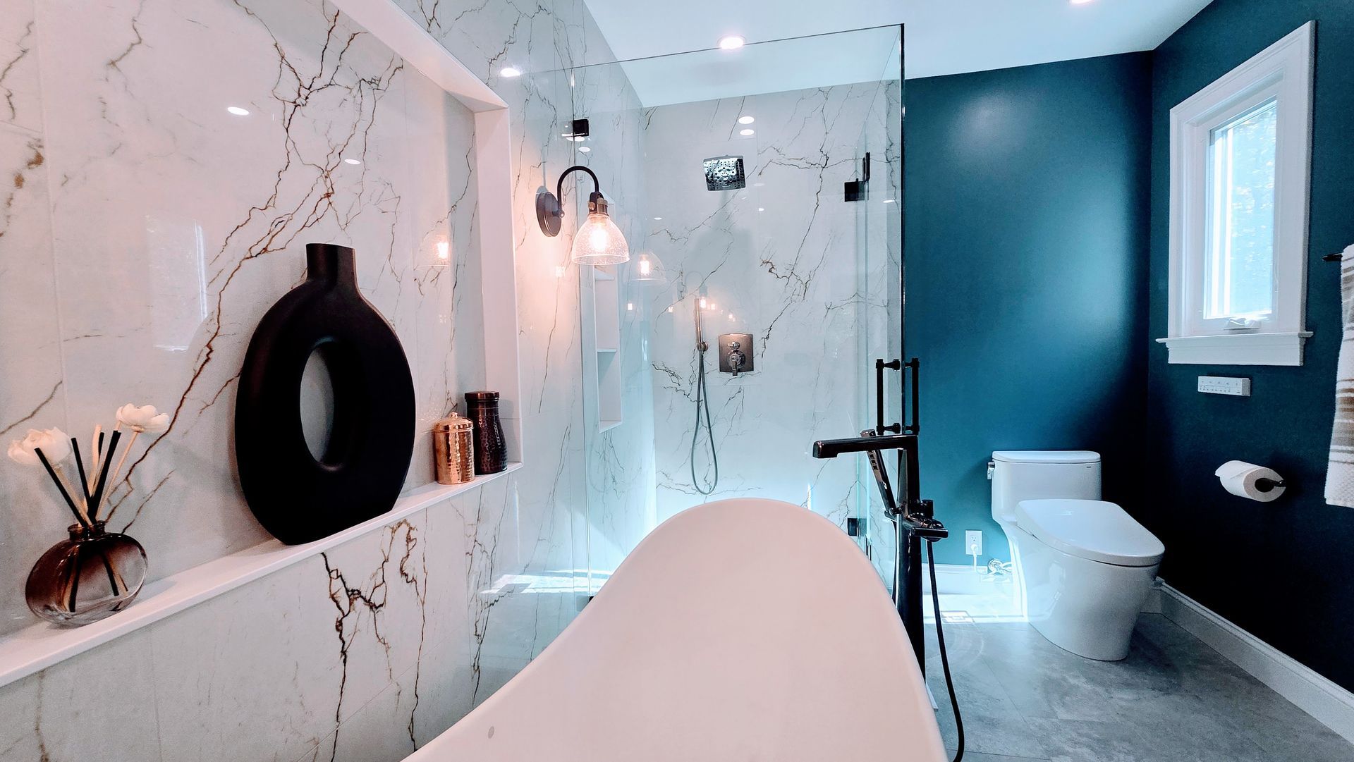 A luxury bathroom remodel in Avon, CT featuring a white marble wall with a standalone tub, dark blue accents, and modern black fixtures.