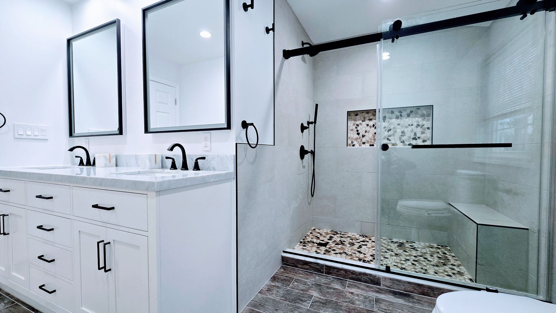 Modern bathroom with white vanity, black fixtures, and glass shower enclosure.