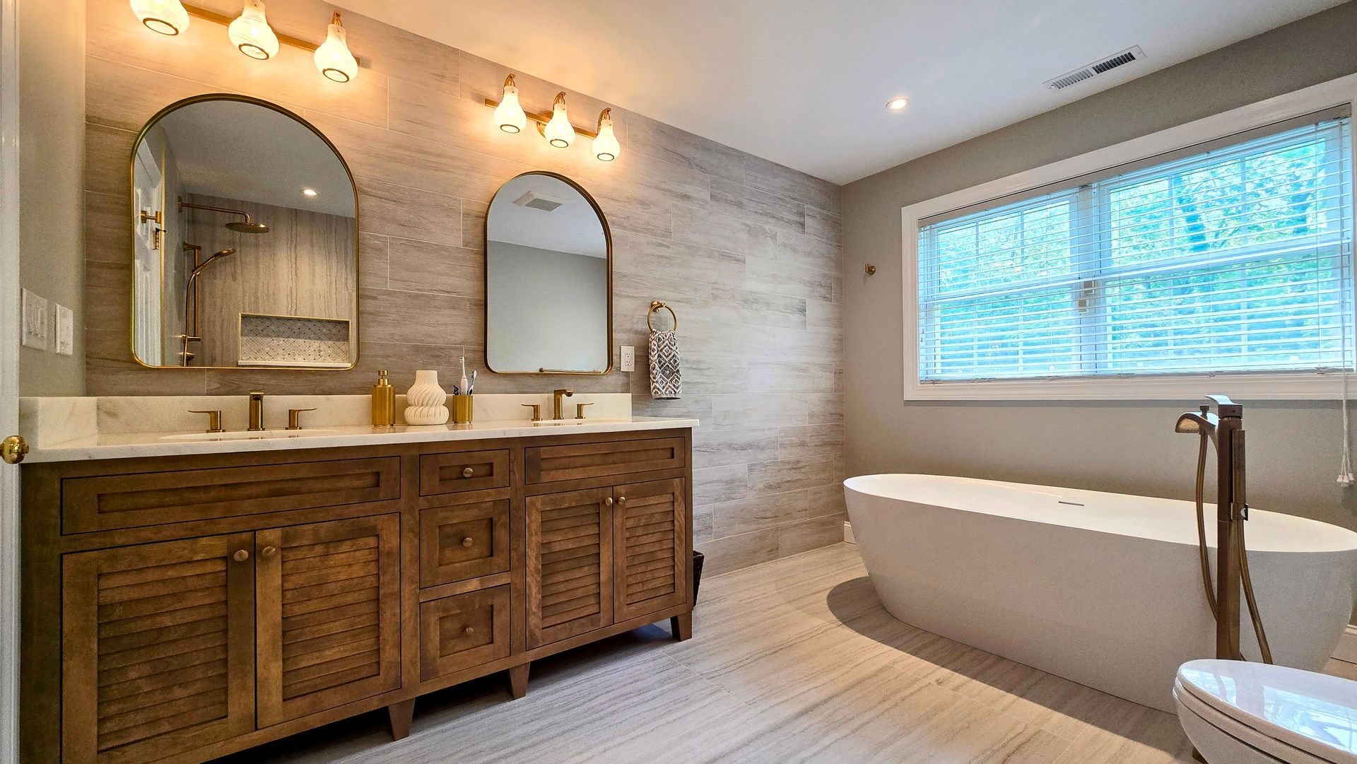 A modern bathroom in Cheshire, CT with a wooden double vanity, two arched mirrors, wood-look wall tiles, and a freestanding white tub.