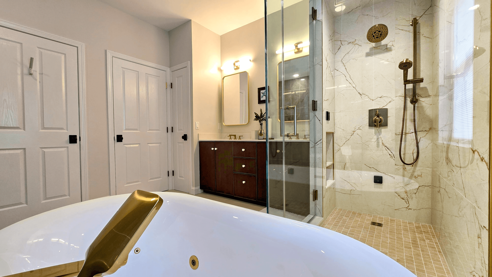 Bright bathroom with a large bathtub, glass shower, white doors, and dark wood cabinet under warm lighting