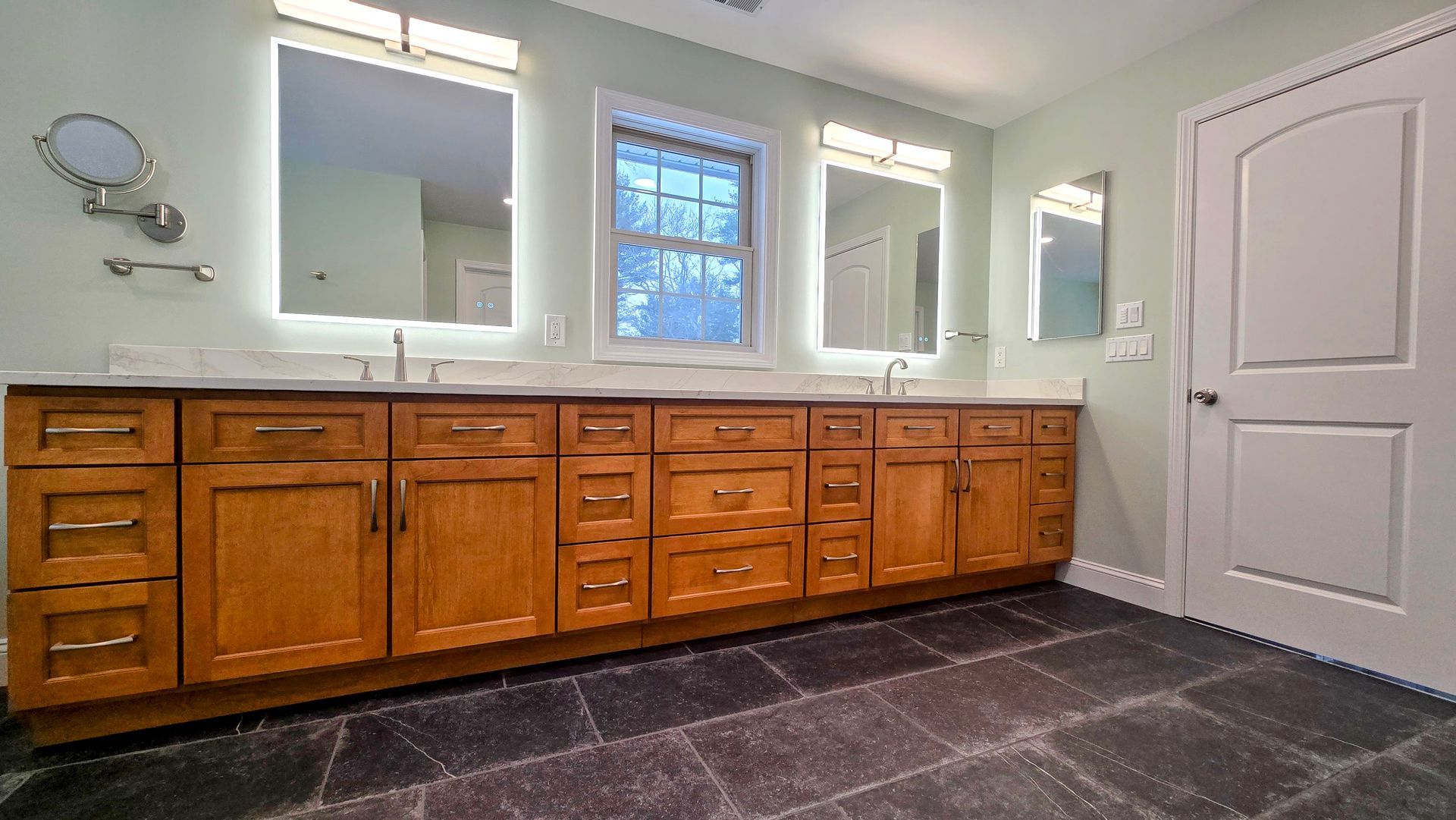 A walk-in shower in Cromwell, CT with vertical, mottled blue tiles, gold fixtures, and a recessed wall niche holding three dark bottles.
