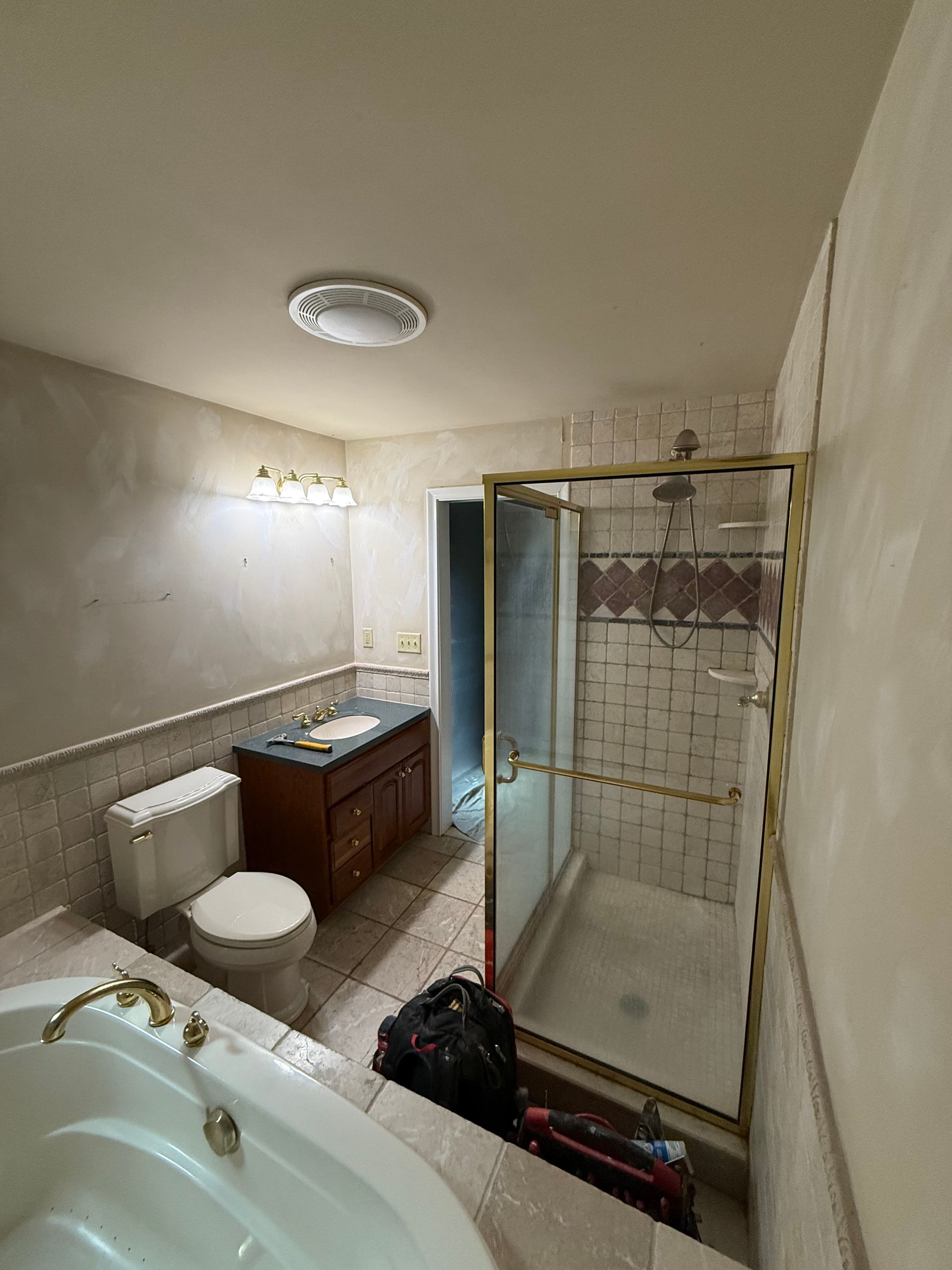 Bathroom with a bathtub, toilet, vanity, and shower. Tan and white tile with gold accents.
