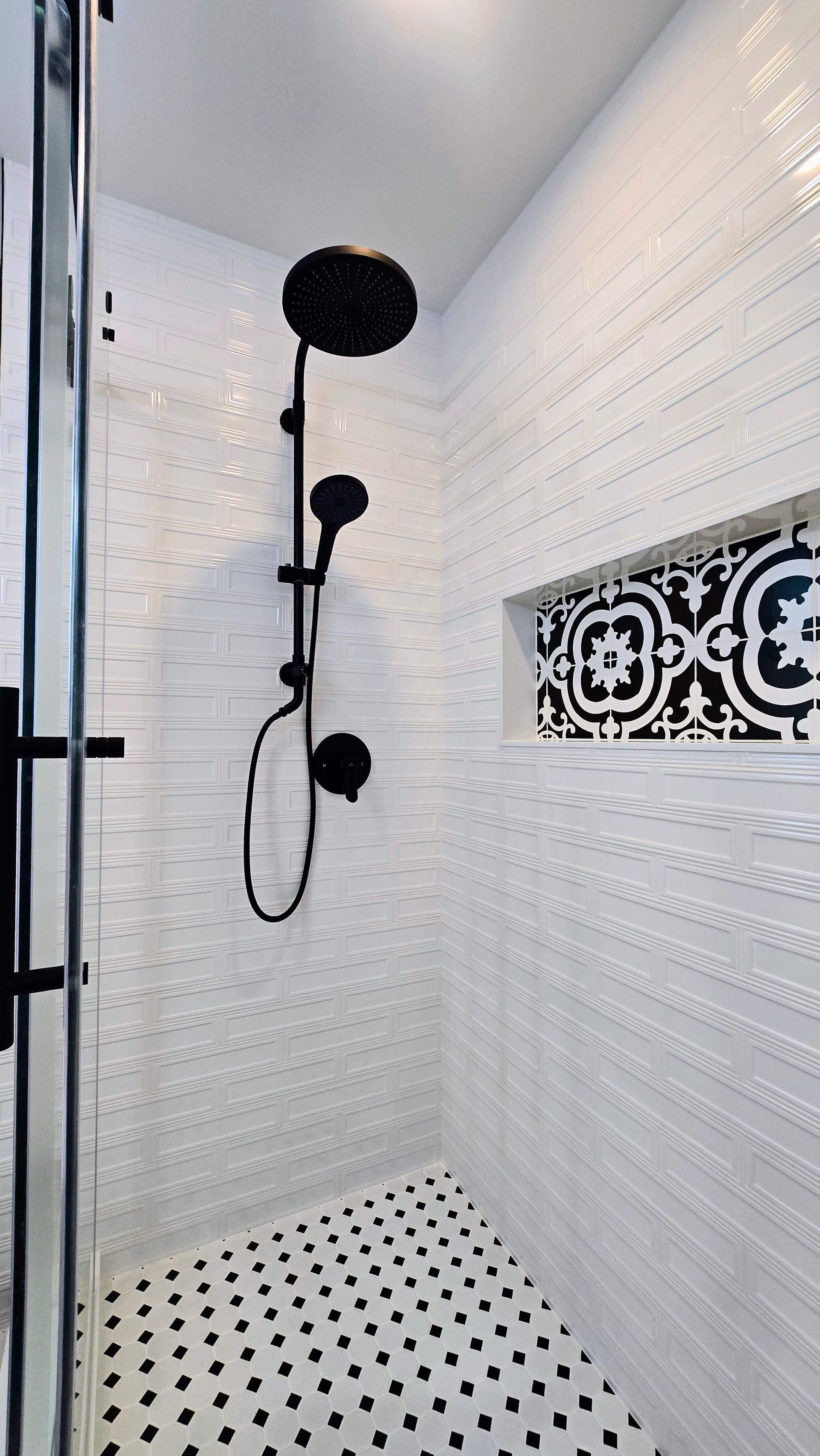 Modern shower remodel in Southington, CT featuring white textured subway tiles, a black rainfall showerhead, and a patterned black-and-white niche.