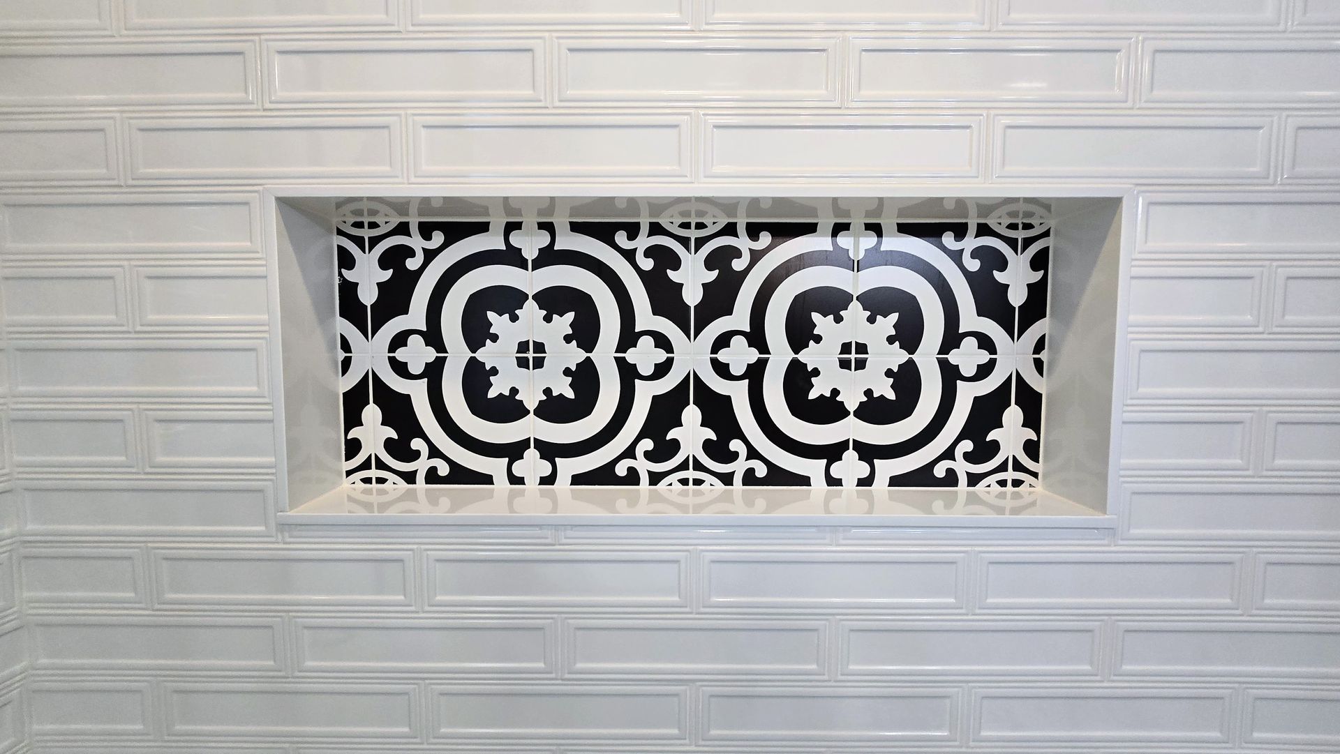 A rectangular shower niche in Southington, CT with a bold, black-and-white decorative tile pattern surrounded by white subway tiles.