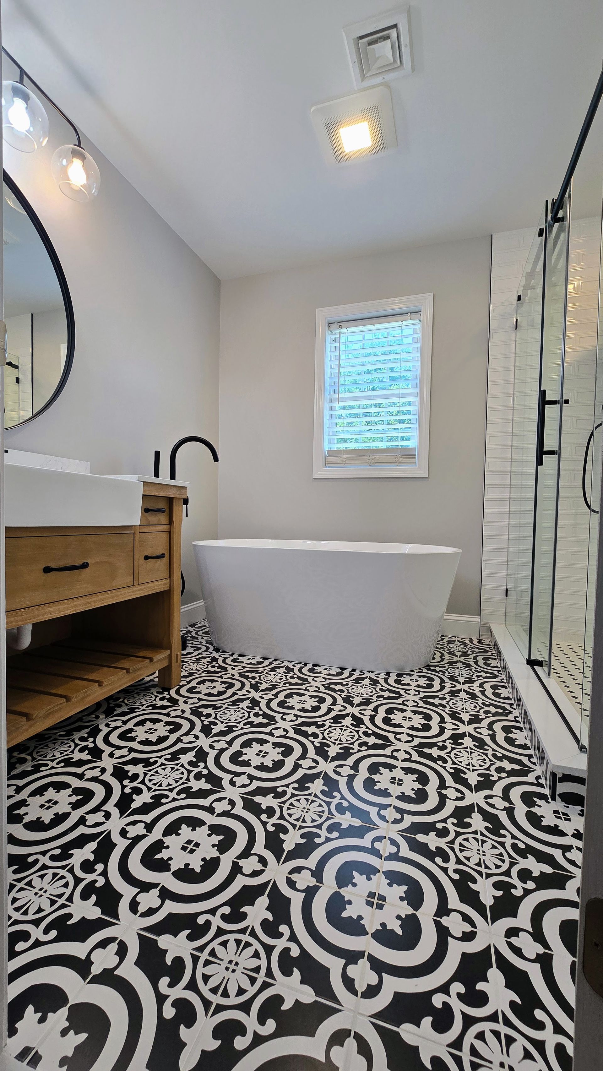 Modern bathroom featuring a soaking tub, a wood vanity with a black faucet, and patterned black-and-white floor tiles.