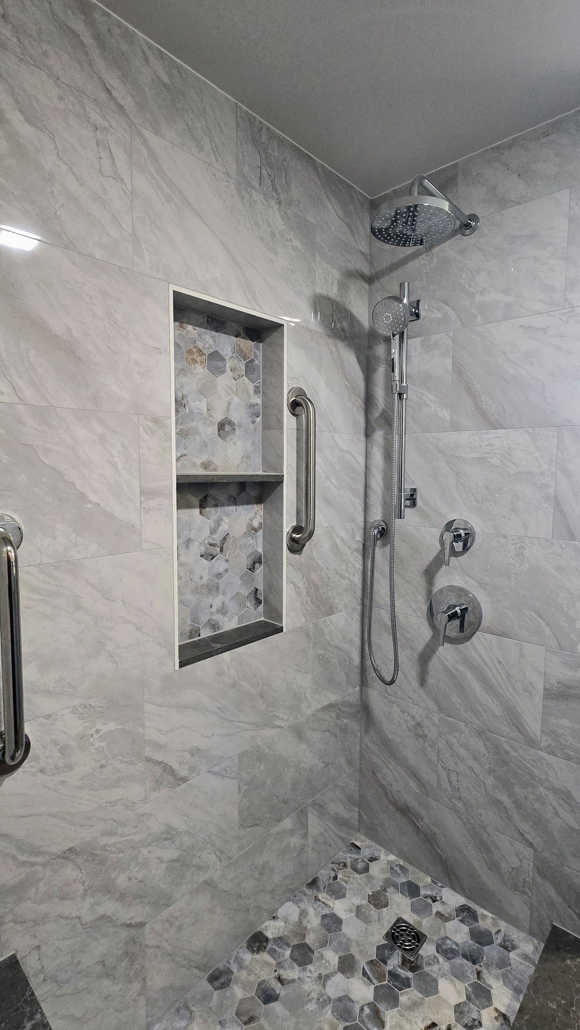 Gray-tiled Southington shower with a built-in shelf, grab bar, and a seat. Chrome shower fixtures.
