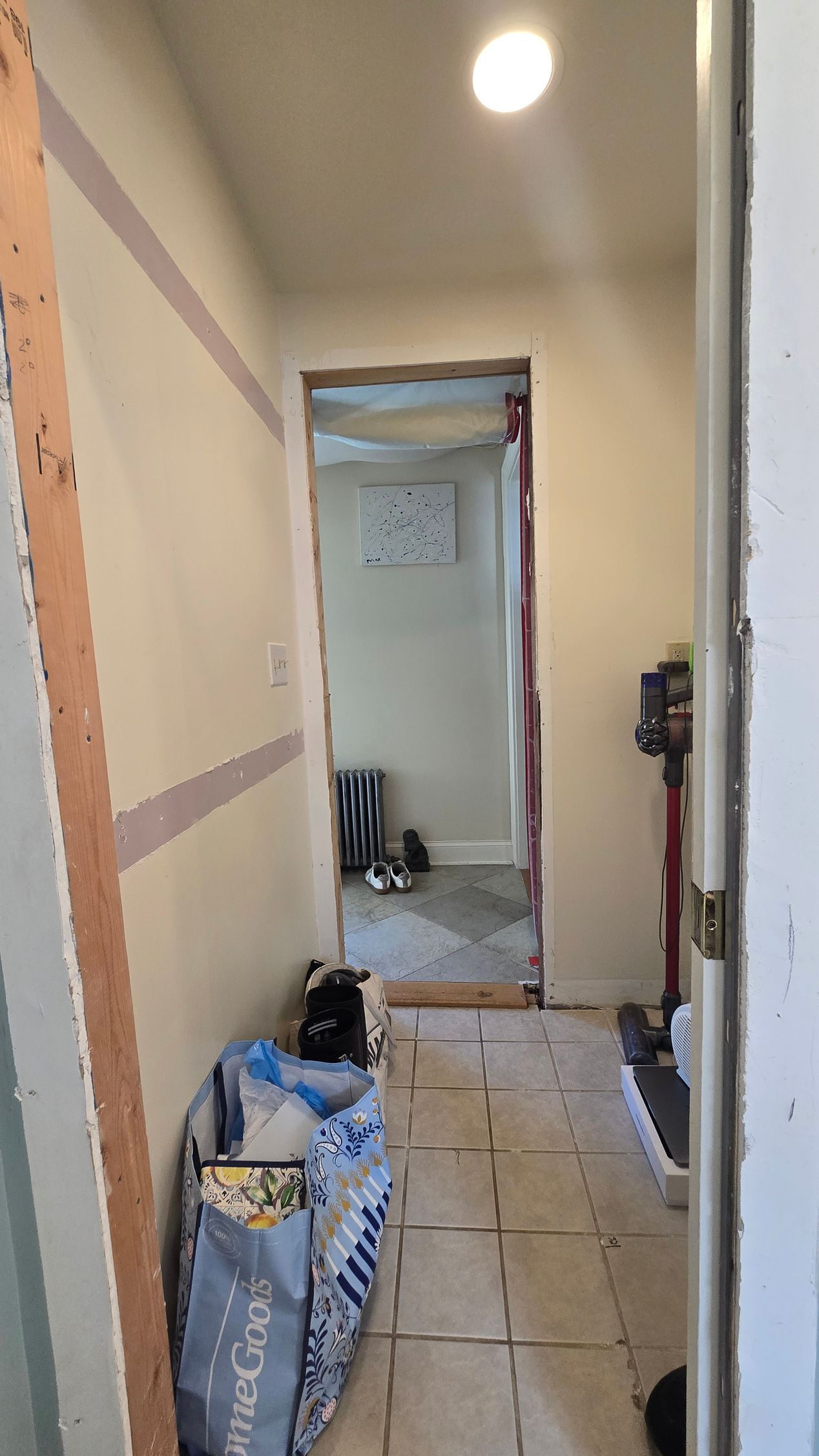 Hallway with open doorway, bags, vacuum, tile floor, and unfinished walls.