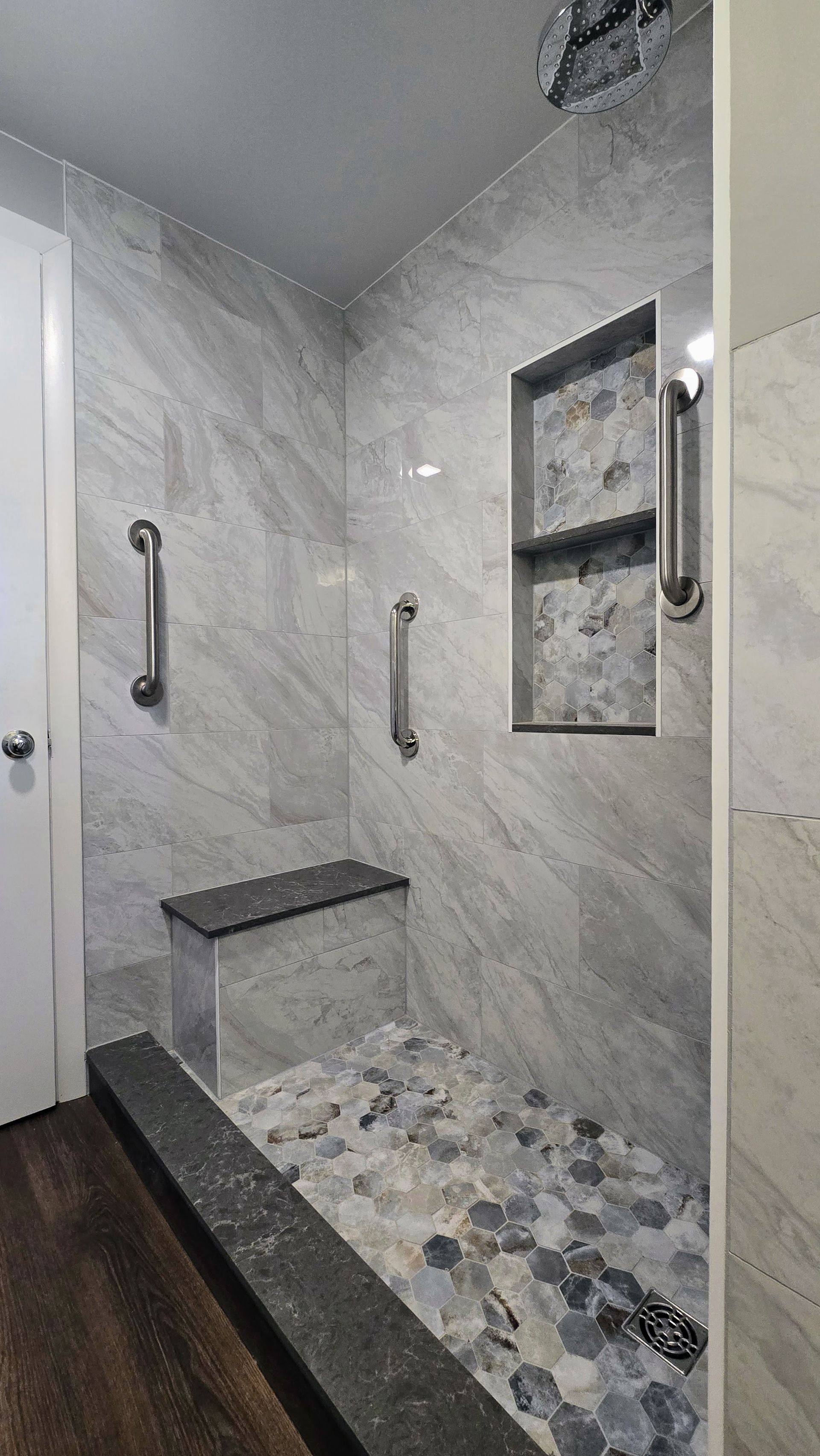 Accessible Southington shower with gray tile, stone floor, built-in bench, and grab bars.