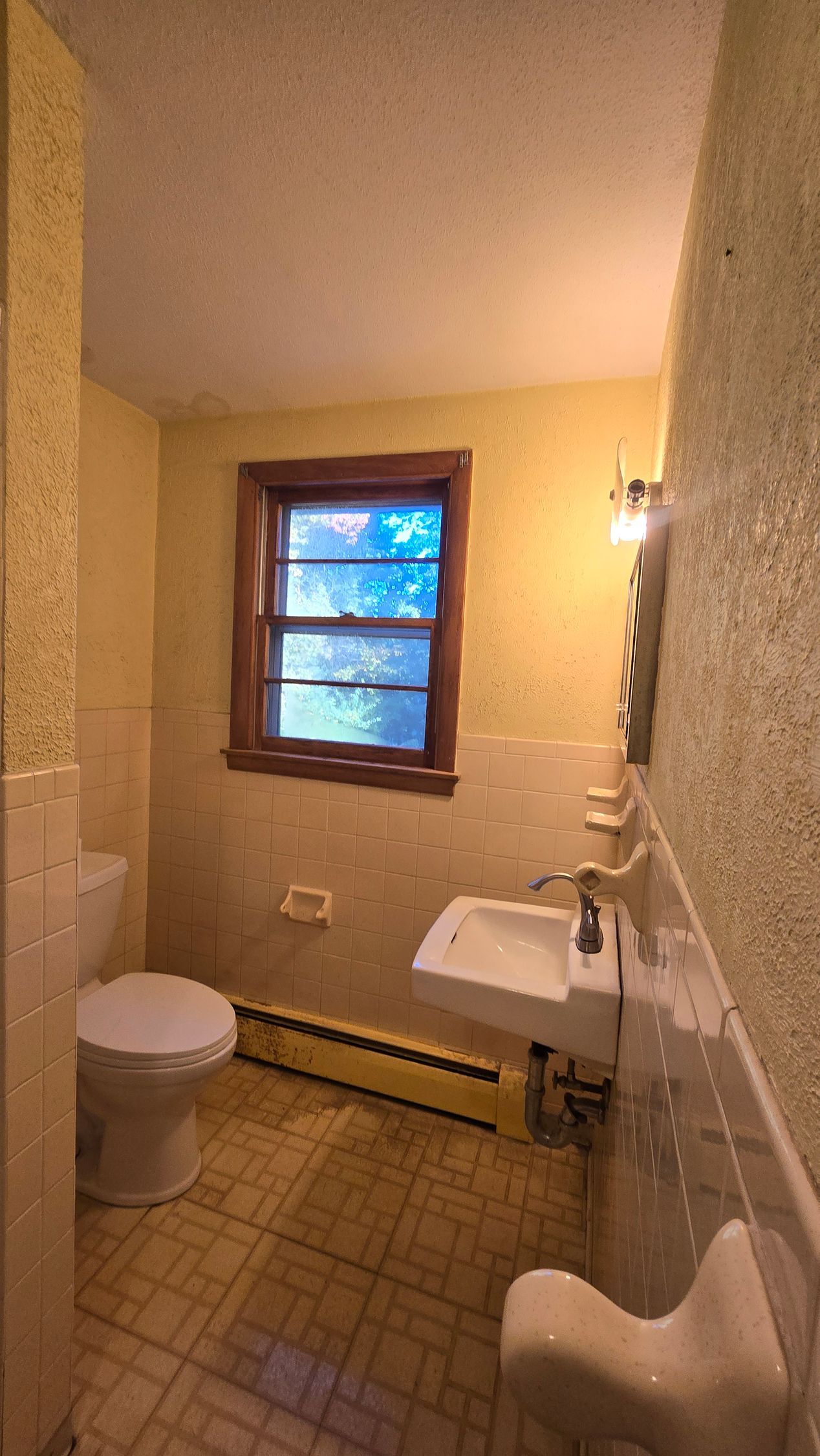 Small Southington bathroom with a toilet, sink, and window. Yellow walls with textured paint and tile.