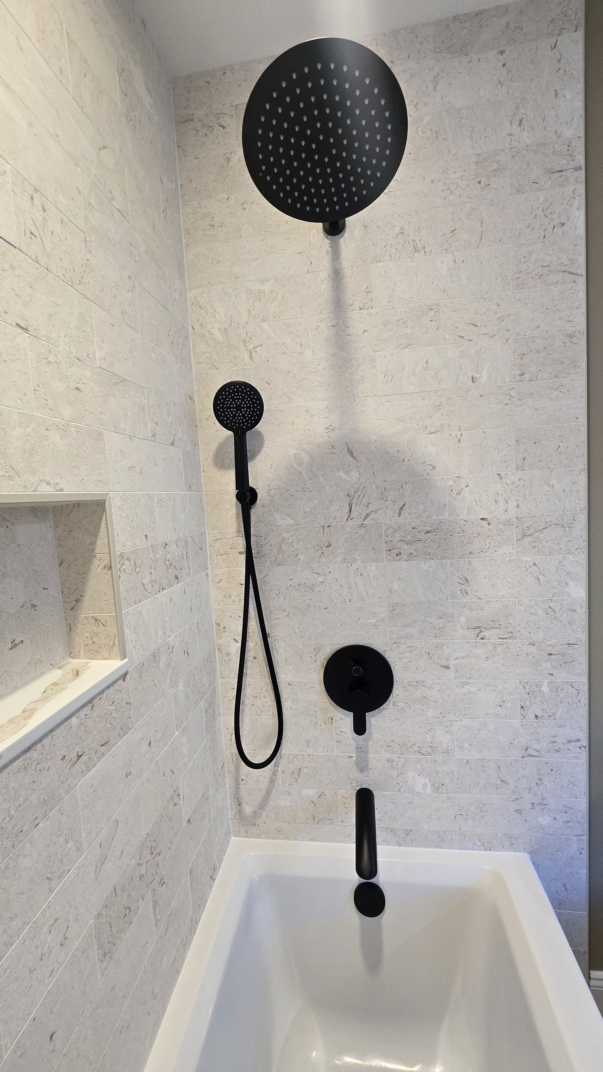 Bristol, CT black shower fixtures in a tiled bathroom; overhead showerhead, hand-held shower, and bathtub.
