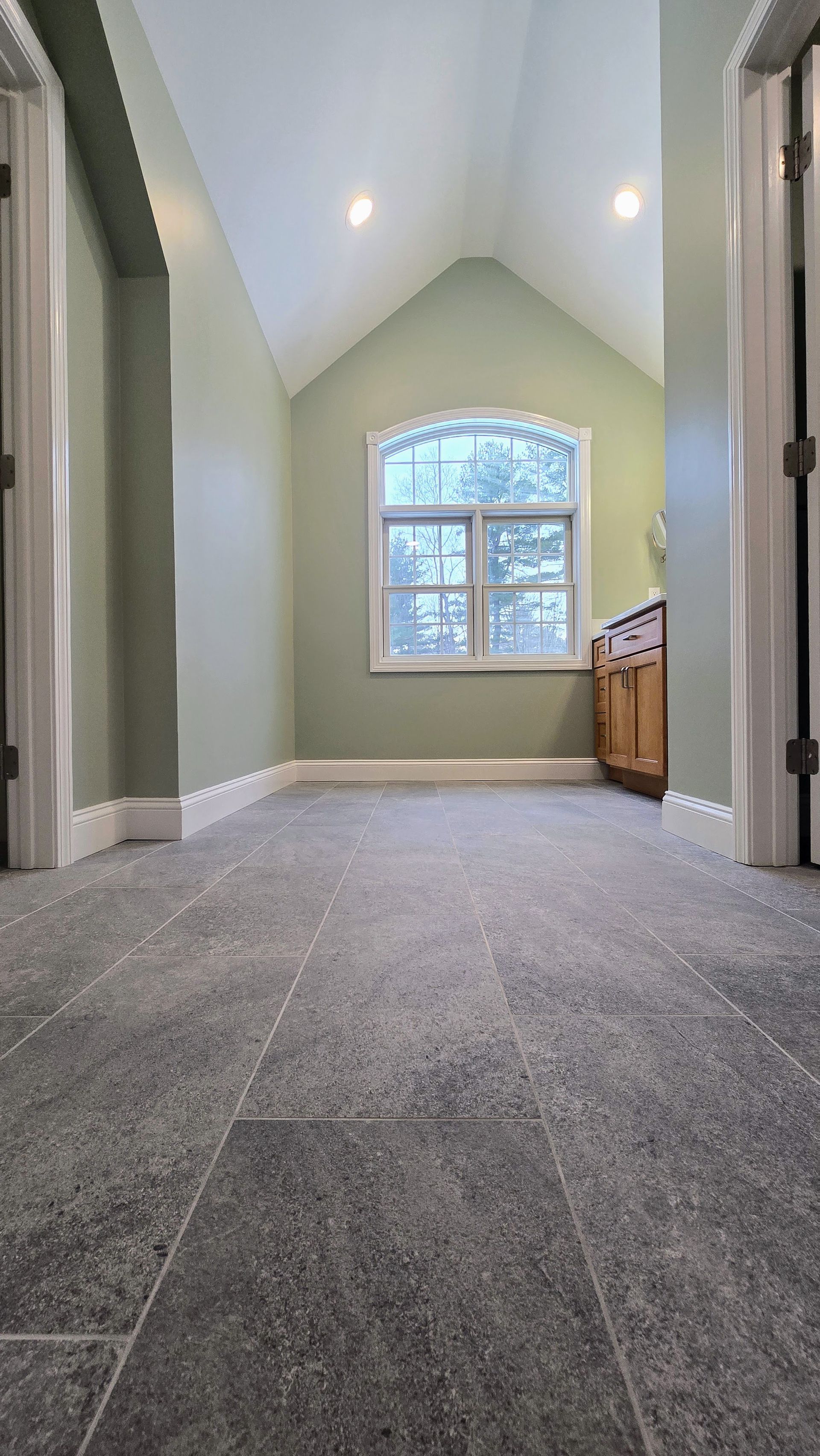 Bathroom in Glastonbury, CT with arched ceiling, green walls, arched window, wood cabinet, grey tiled floor.