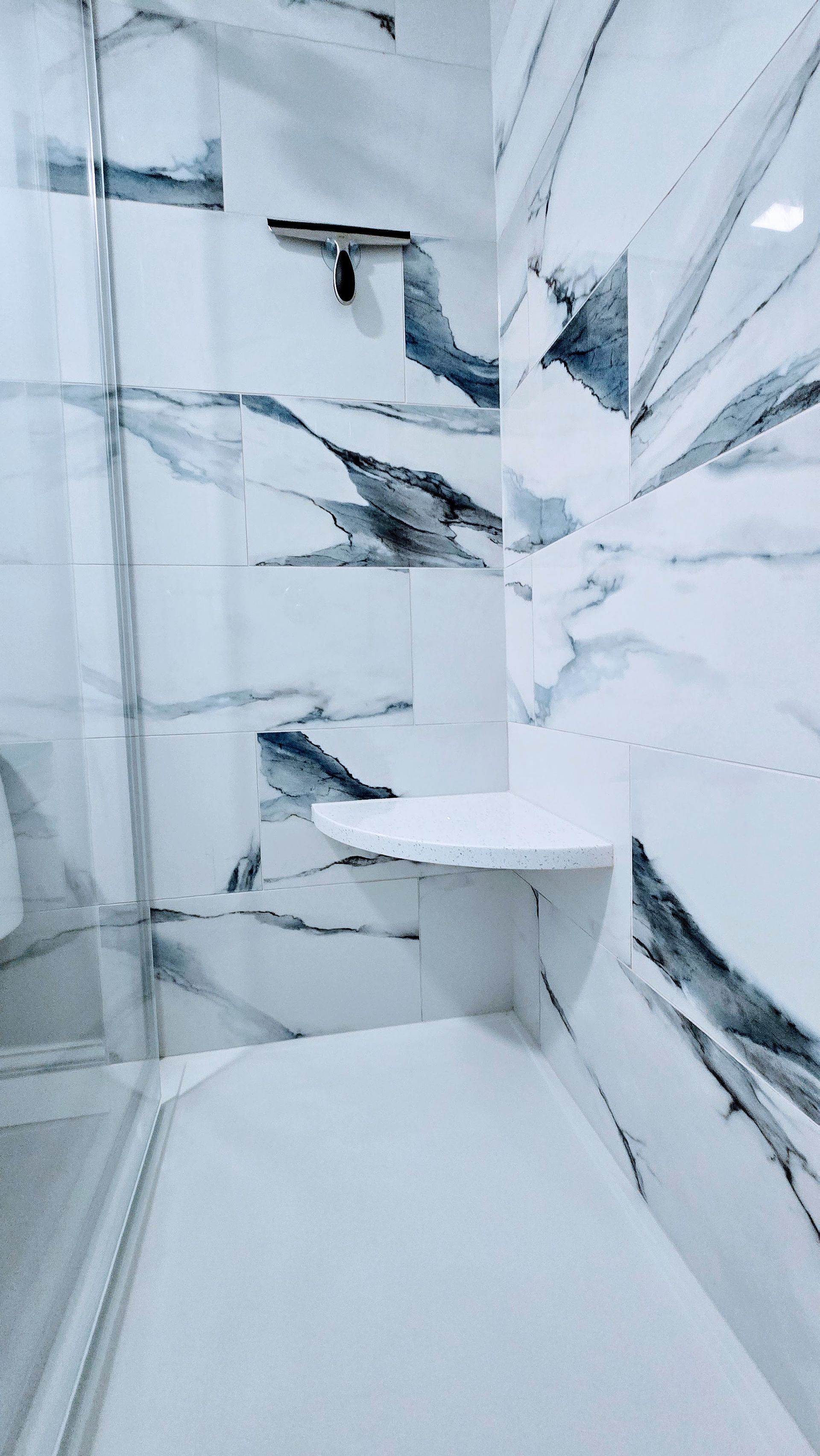 White marble-tiled shower with a built-in shelf and a squeegee.