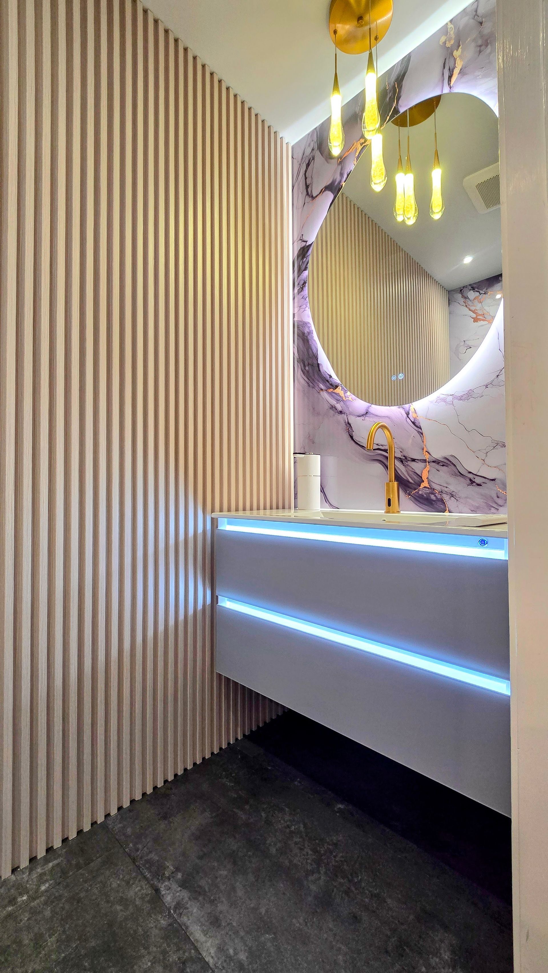 Modern powder room in Simsbury, CT with wood paneling, purple marble accent wall, floating vanity, gold fixtures, and round mirror.
