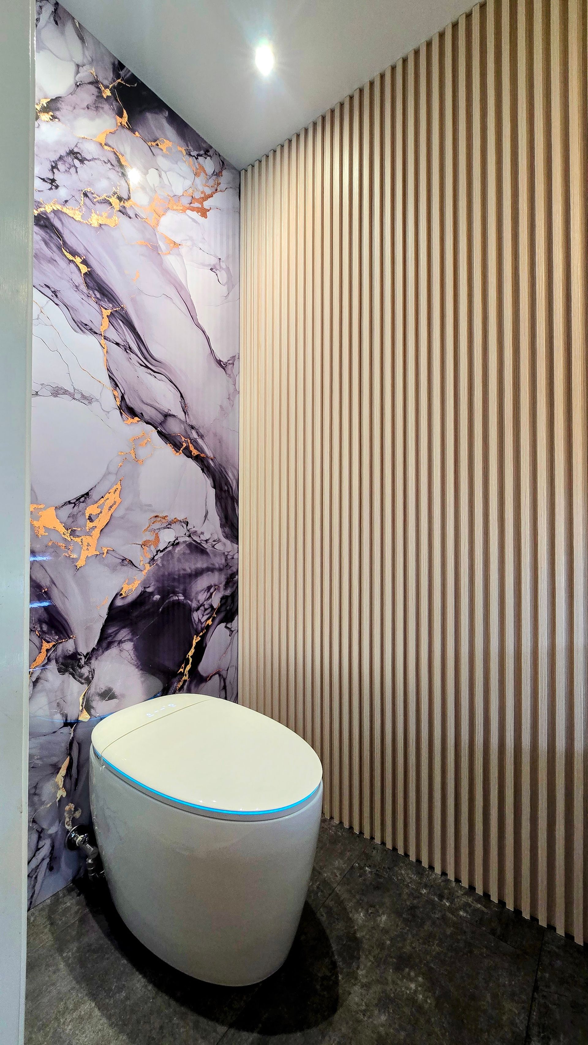 A modern smart toilet in a small powder room in Simsbury, CT with marble and wood paneling walls.