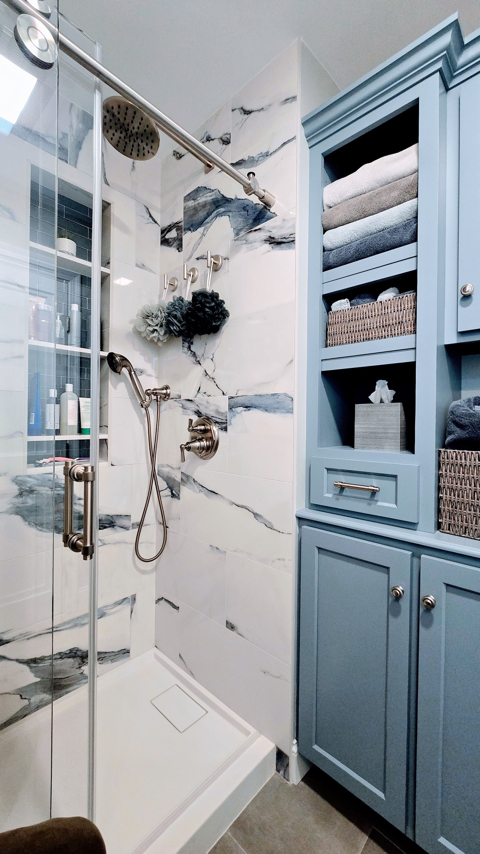 Blue and white West Hartford bathroom with a shower and cabinet filled with towels.