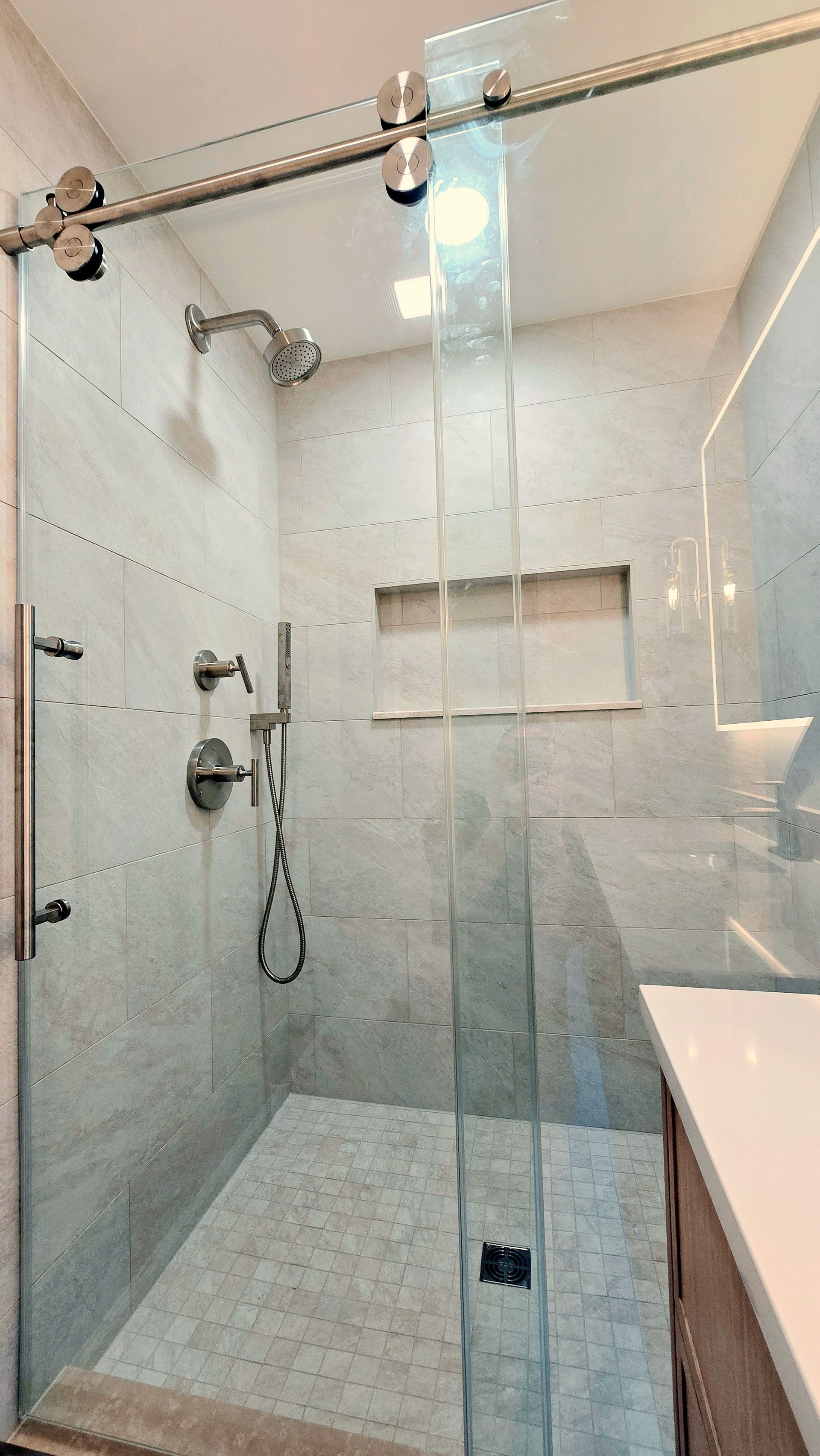 A walk-in shower in Simsbury, CT with a glass sliding door, light-colored tile walls, a built-in recessed niche, and a chrome shower head.