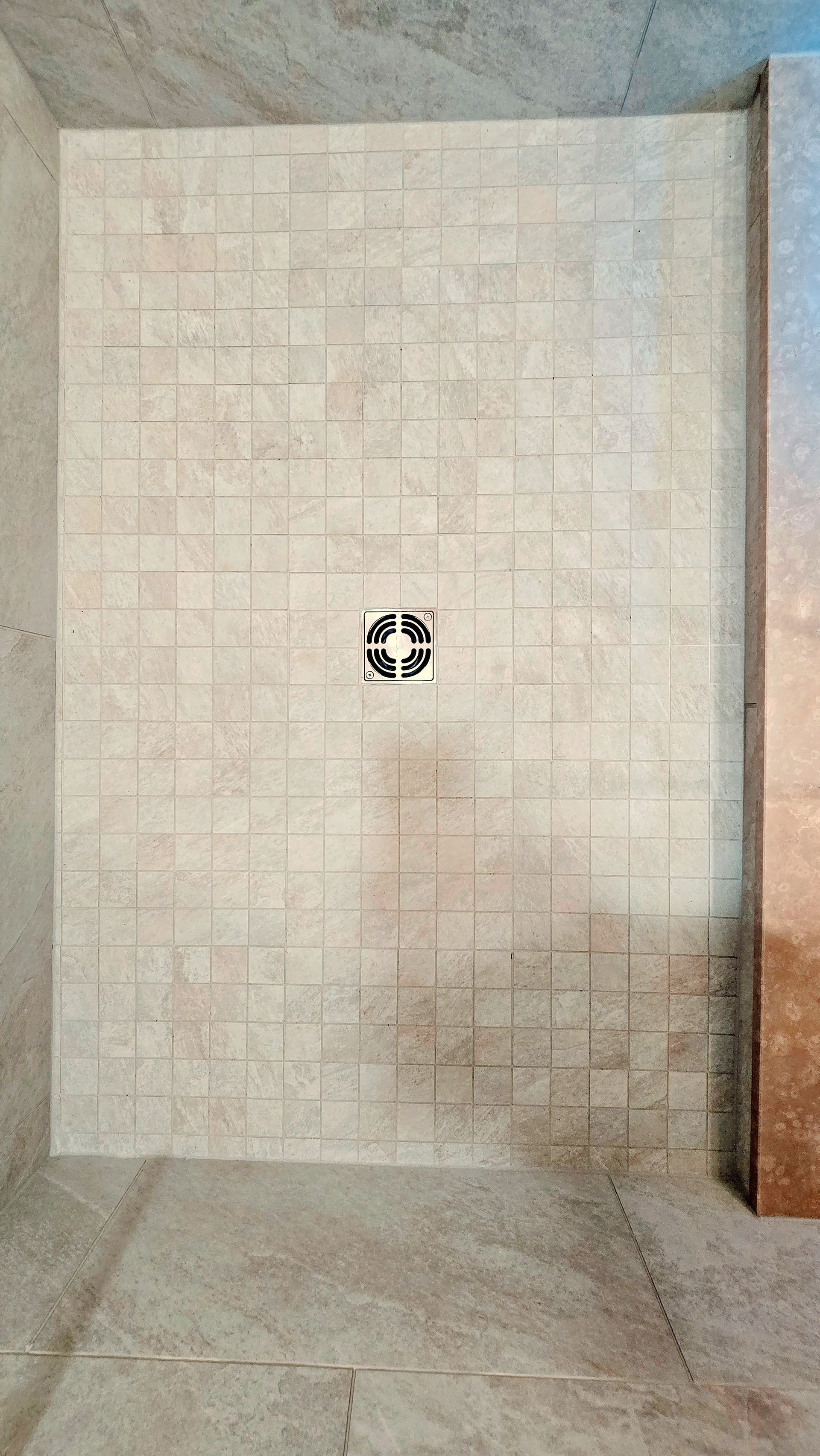 A tiled shower floor with a single centered chrome drain or fixture in Simsbury, CT, featuring a light tan, geometric grid pattern.