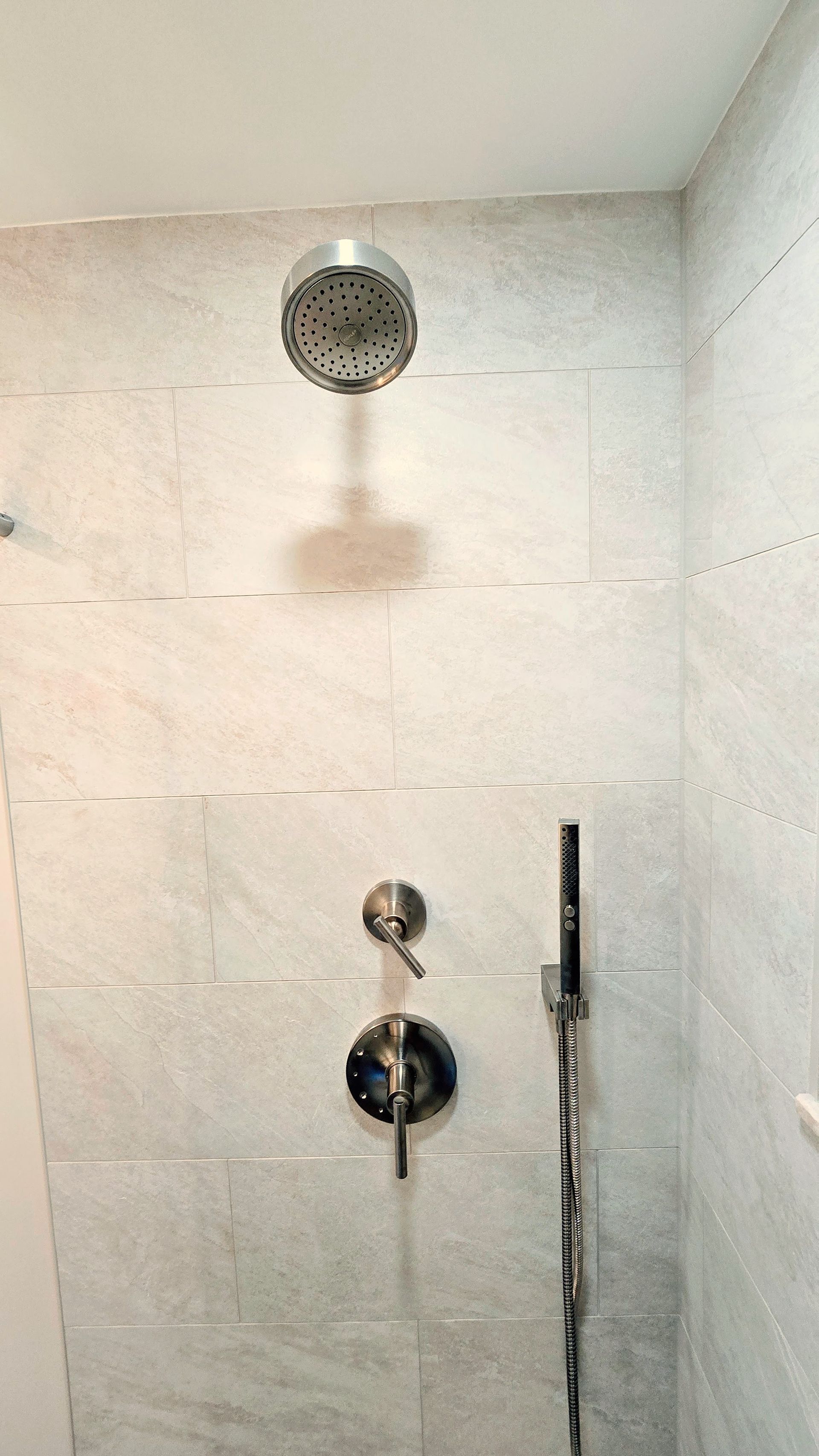 A shower in Simsbury, CT with interior with light gray marble tiles, a circular showerhead, and dual silver control handles on the wall.